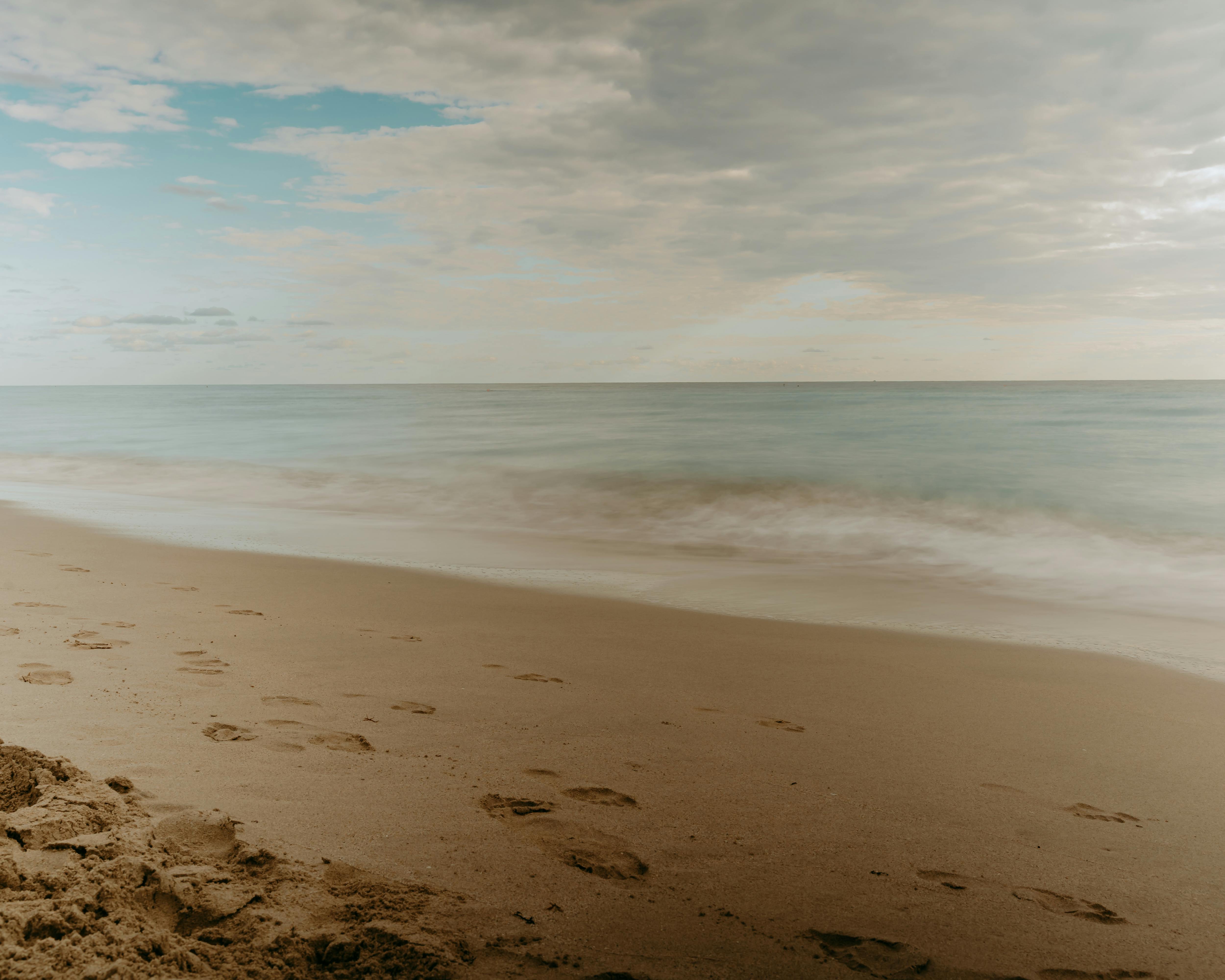 無料 穏やかな波と砂浜の足跡が、懐かしさと穏やかさを呼び起こす静かなビーチの風景。 写真素材