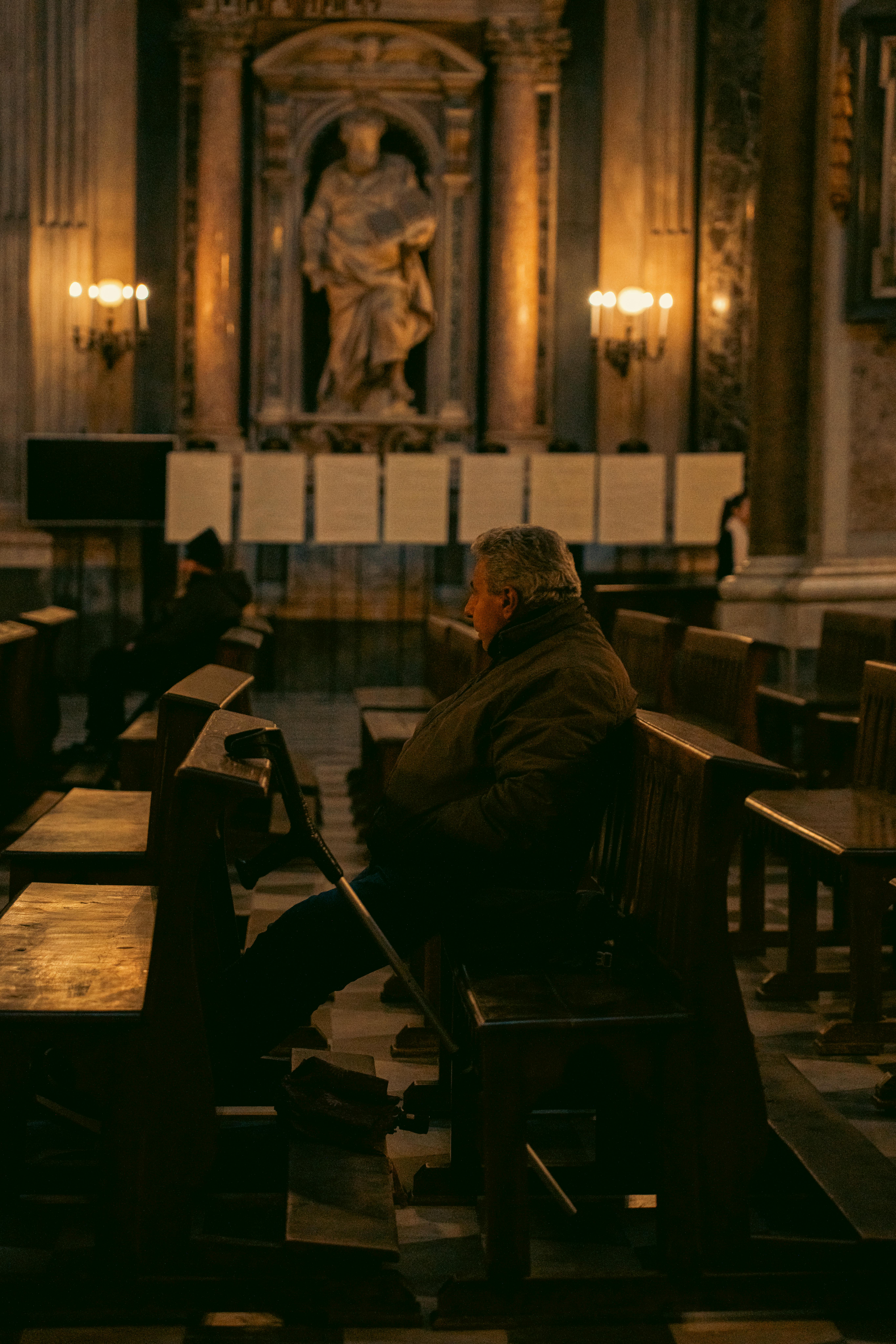 бесплатная Мужчина сидит в тихом задумчивом настроении на деревянных скамьях в тускло освещенной исторической церкви в Неаполе, Италия. Стоковое фото