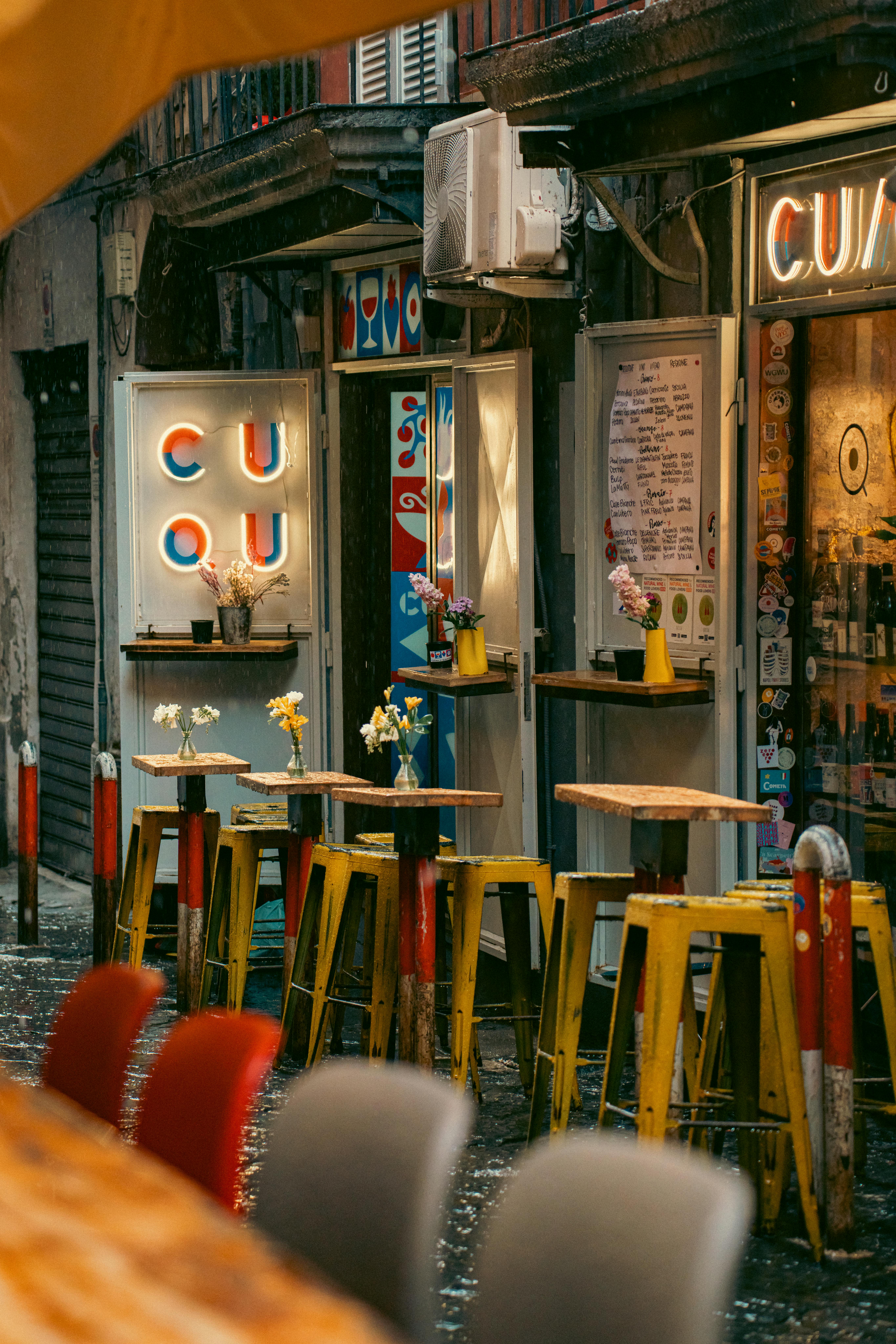 Kostenlos Gemütliches Straßencafé mit bunten Barhockern und Leuchtreklamen in Neapel, Italien. Stock-Foto