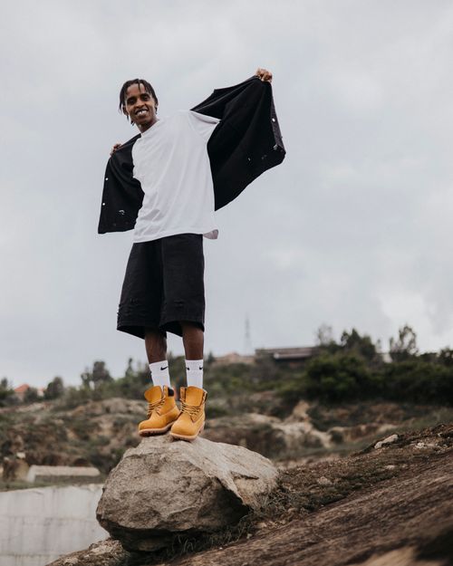Free Young man poses confidently on a rock, wearing casual clothing, outdoors under a cloudy sky. Stock Photo