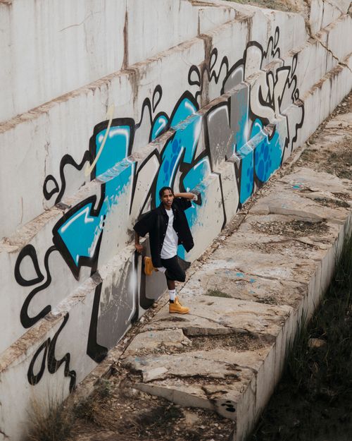 Free Man standing beside vibrant graffiti on concrete structure, showcasing urban art. Stock Photo