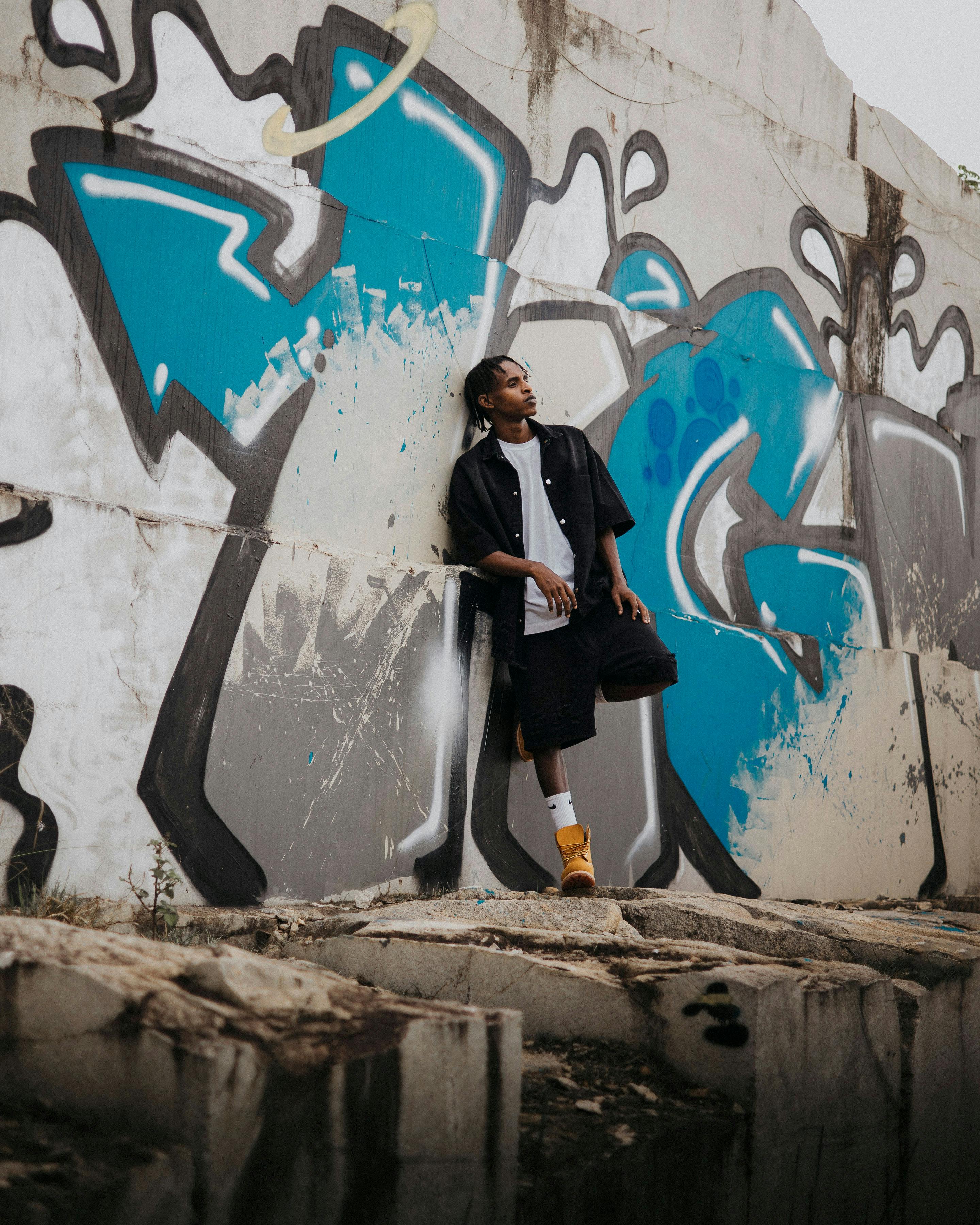 Free Portrait of young adult leaning against graffiti-covered wall in an urban setting. Stock Photo