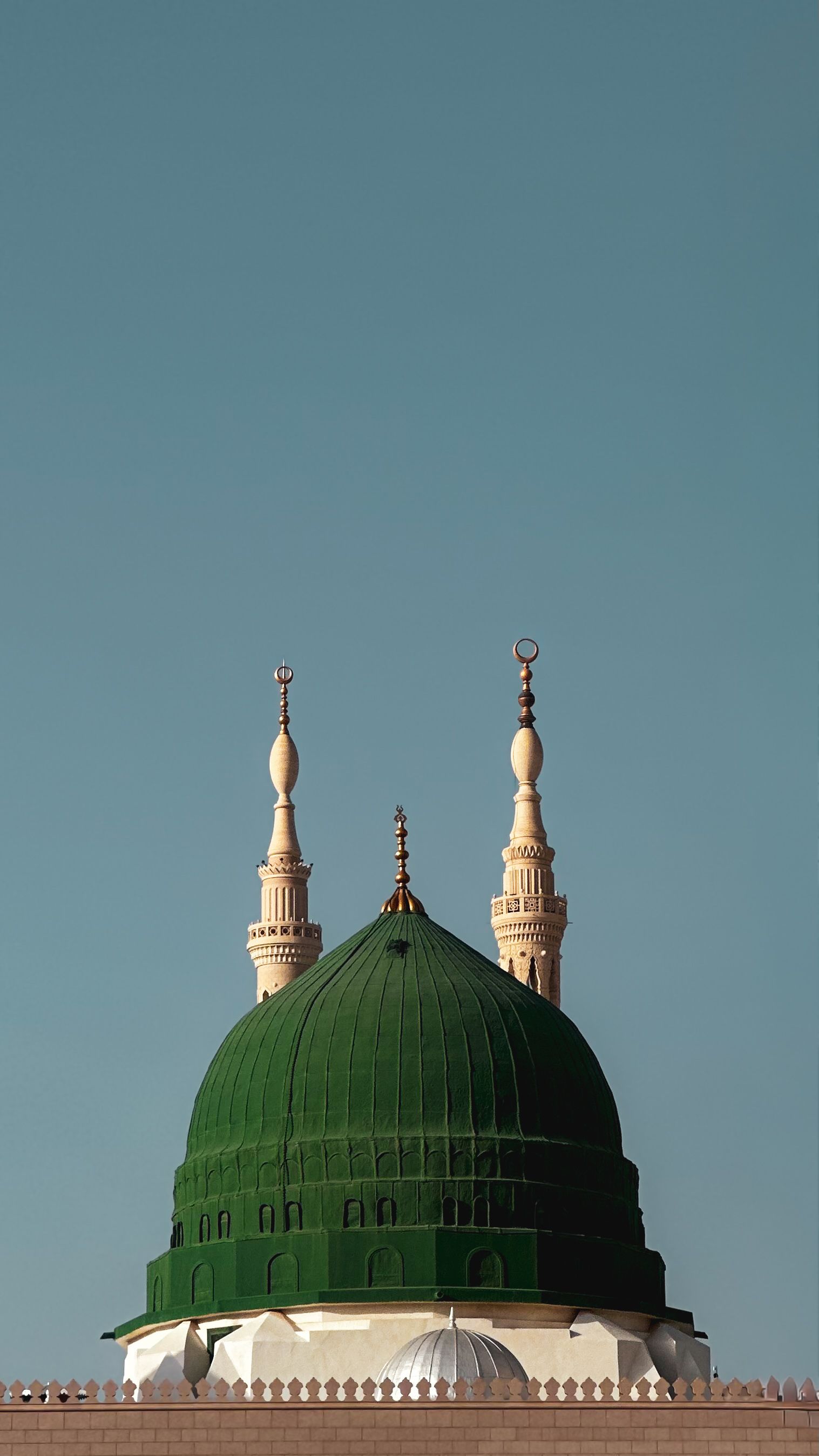 Majestic view of the Green Dome and minarets of Al-Masjid an-Nabawi against a clear blue sky in Medina, Saudi Arabia.