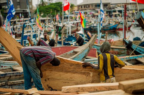 Free Fishermen repairing wooden boats at Tema harbor, highlighting traditional craftsmanship in Ghana. Stock Photo