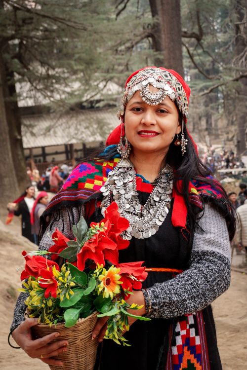 Free Woman in colorful traditional attire holding a basket of vibrant flowers outdoors. Stock Photo
