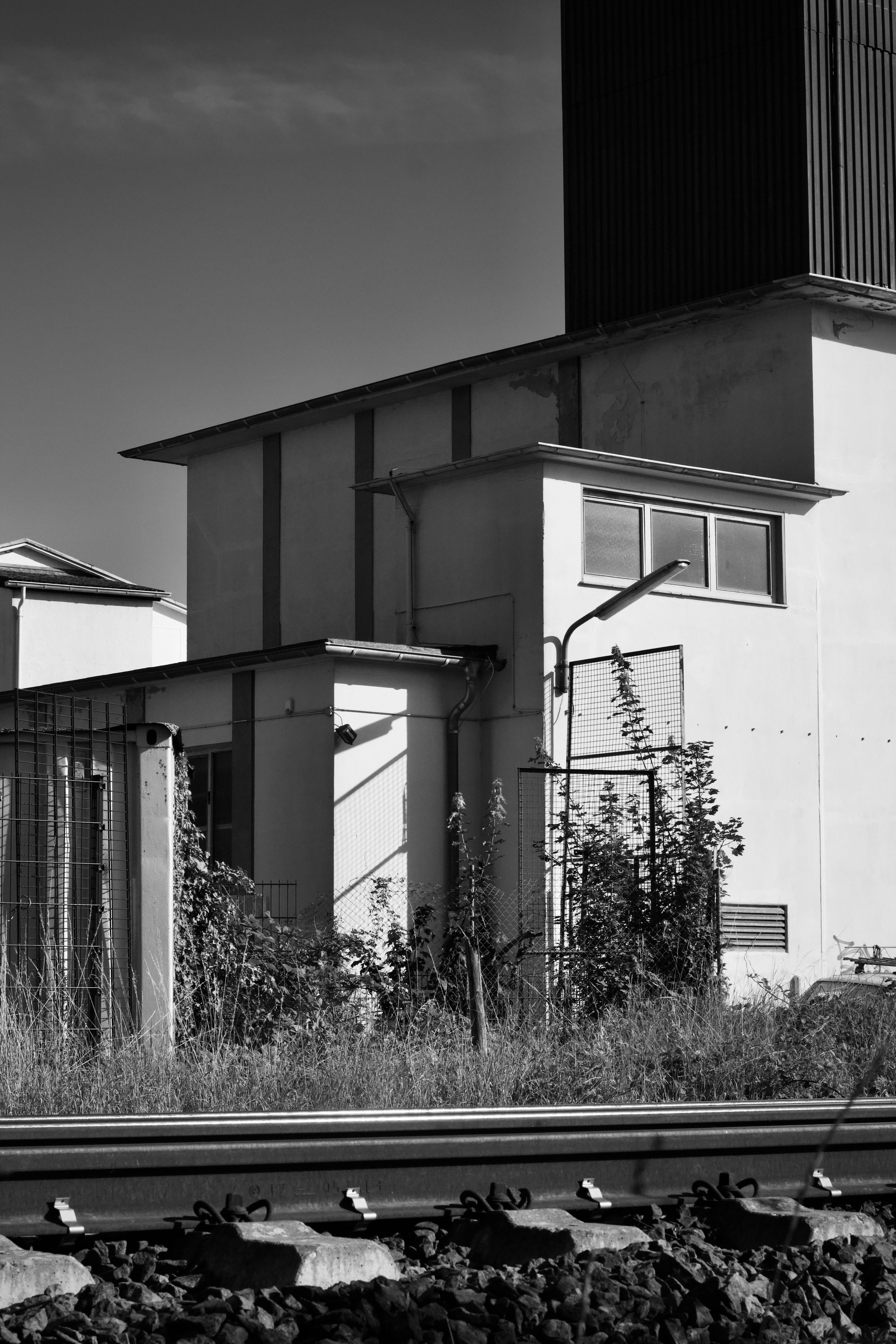 Gratis Monokromt bilde av en moderne industribygning bak jernbanespor i dagslys. Arkivbilde