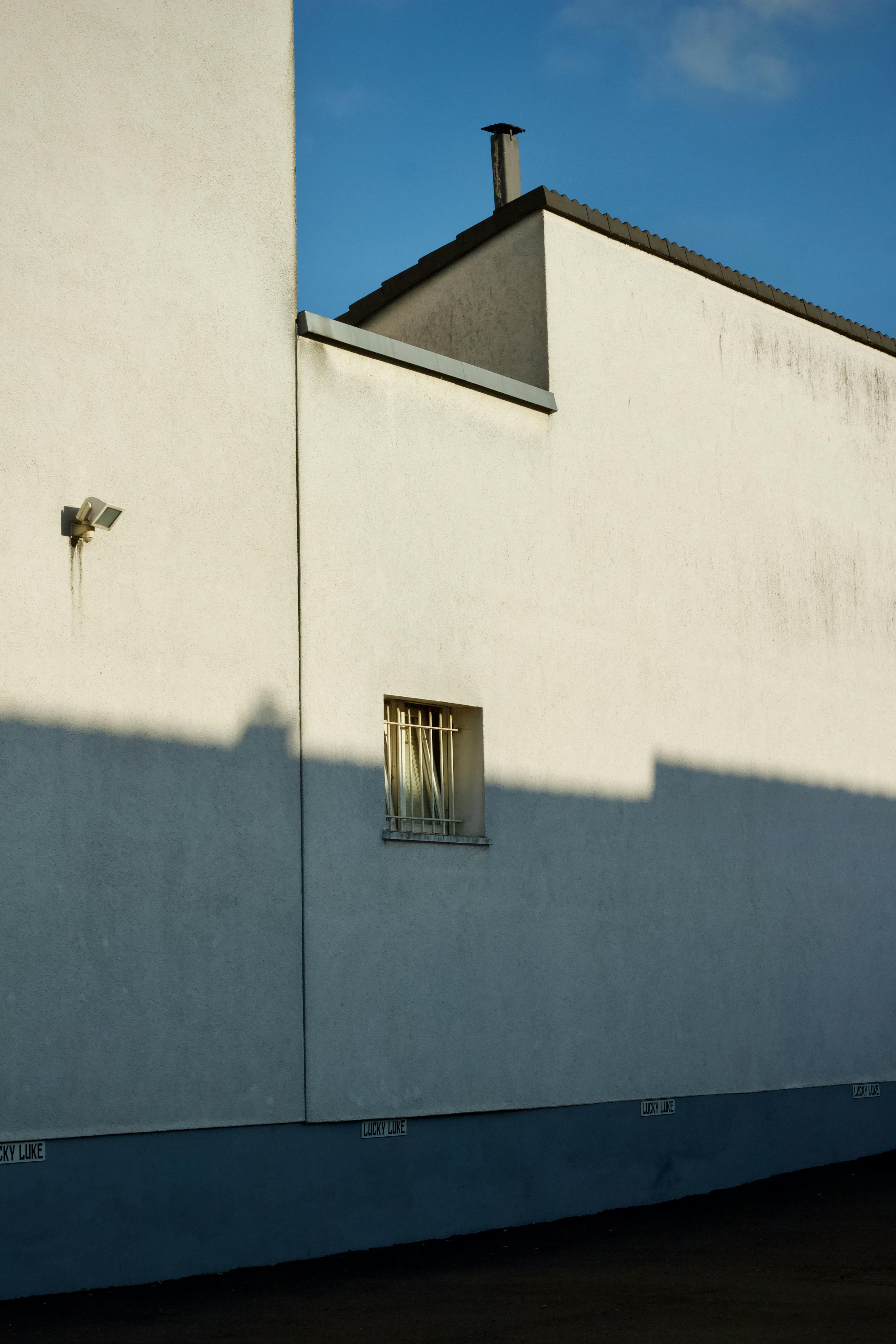 Gratis En minimalistisk bygningsfacade, der fremviser skygger og lys i et boligområde med klar blå himmel. Lagerfoto