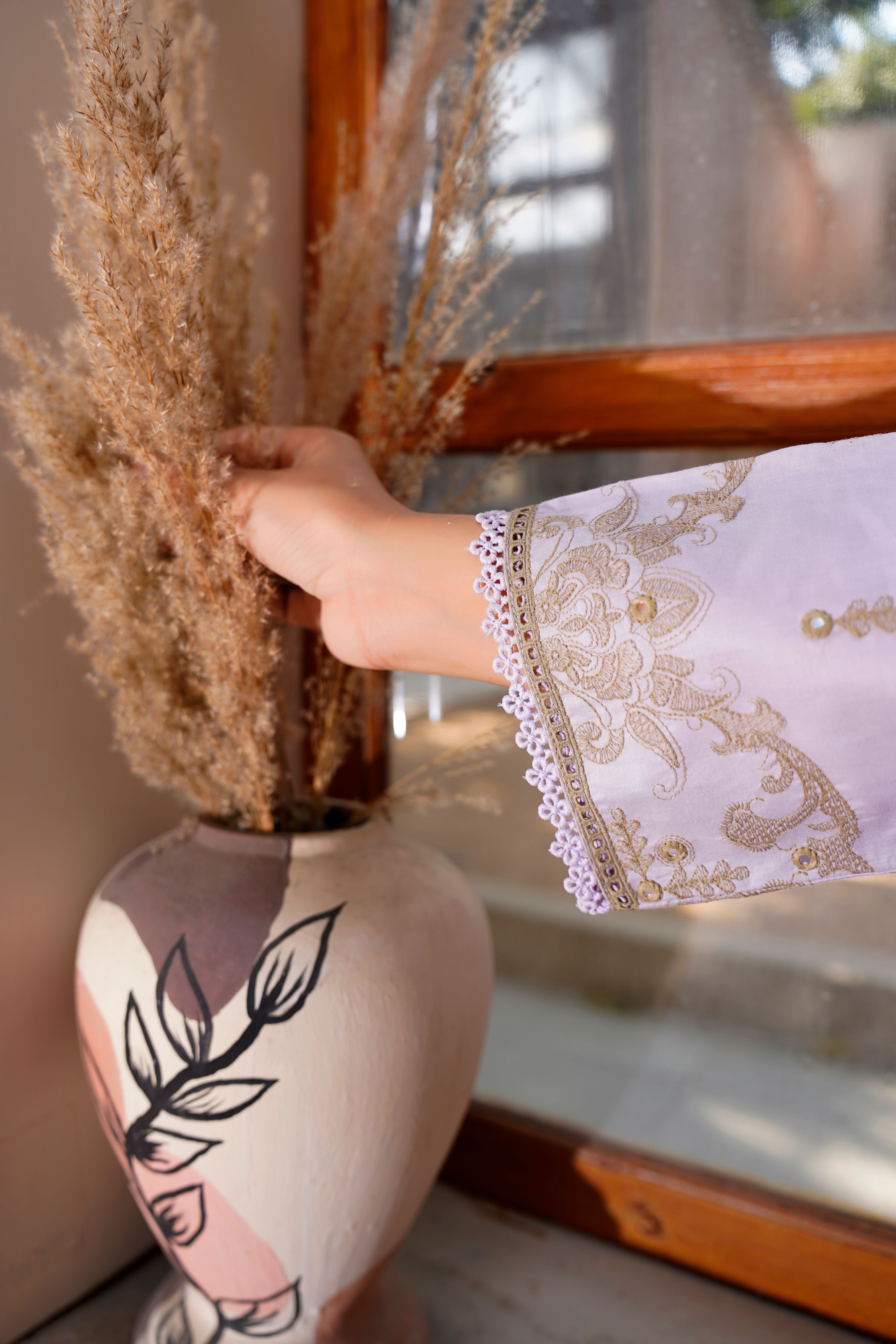 A hand arranges dried flowers in an artistic vase, showcasing intricate embroidered sleeve design.