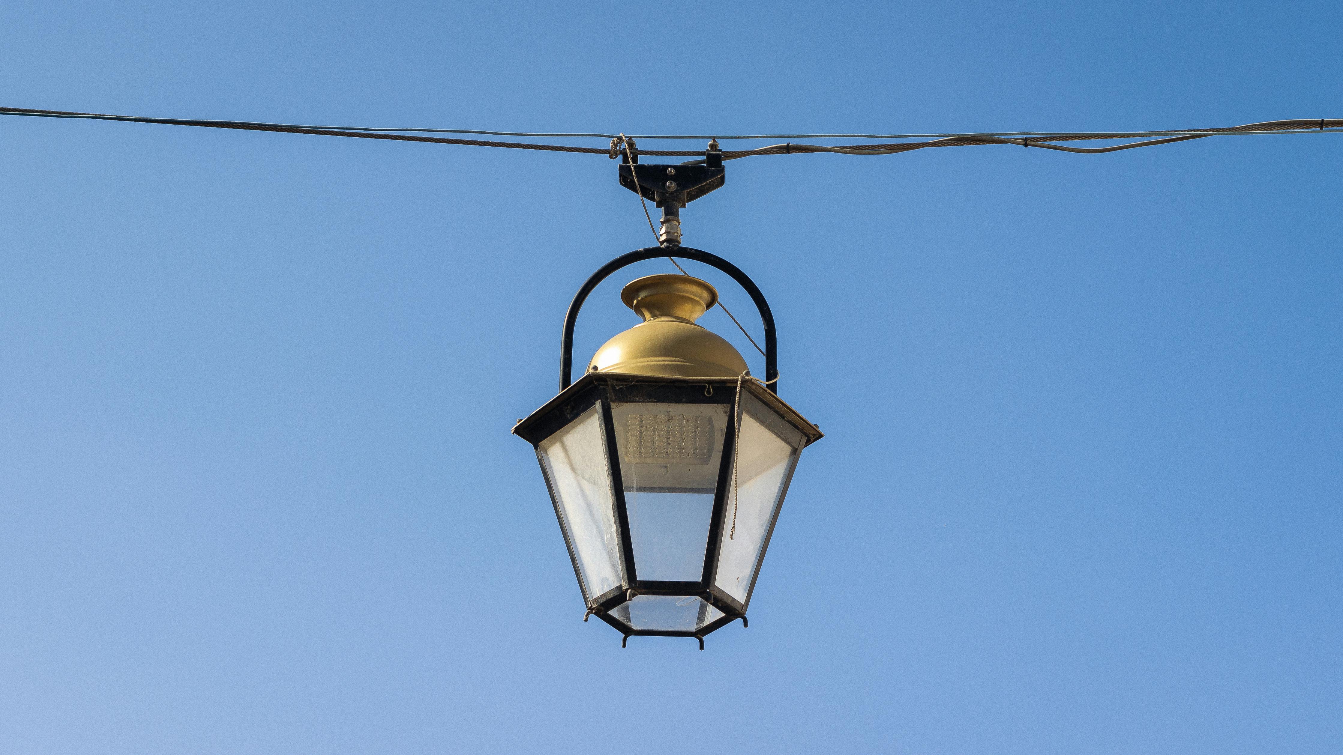 Free A classic streetlamp suspended on wires against a bright blue sky, showcasing vintage design. Stock Photo