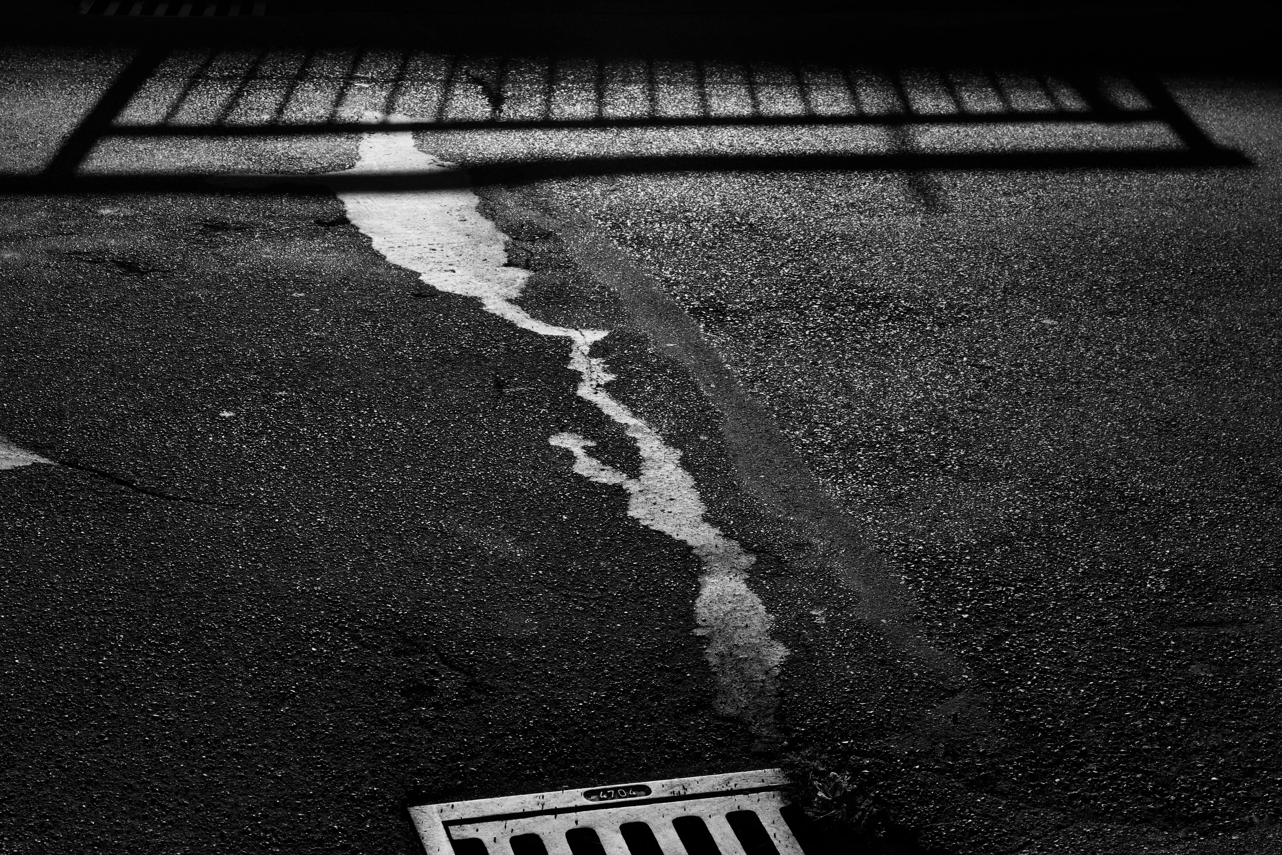 Free Black and white image of a shadow pattern on urban pavement with a drain. Stock Photo