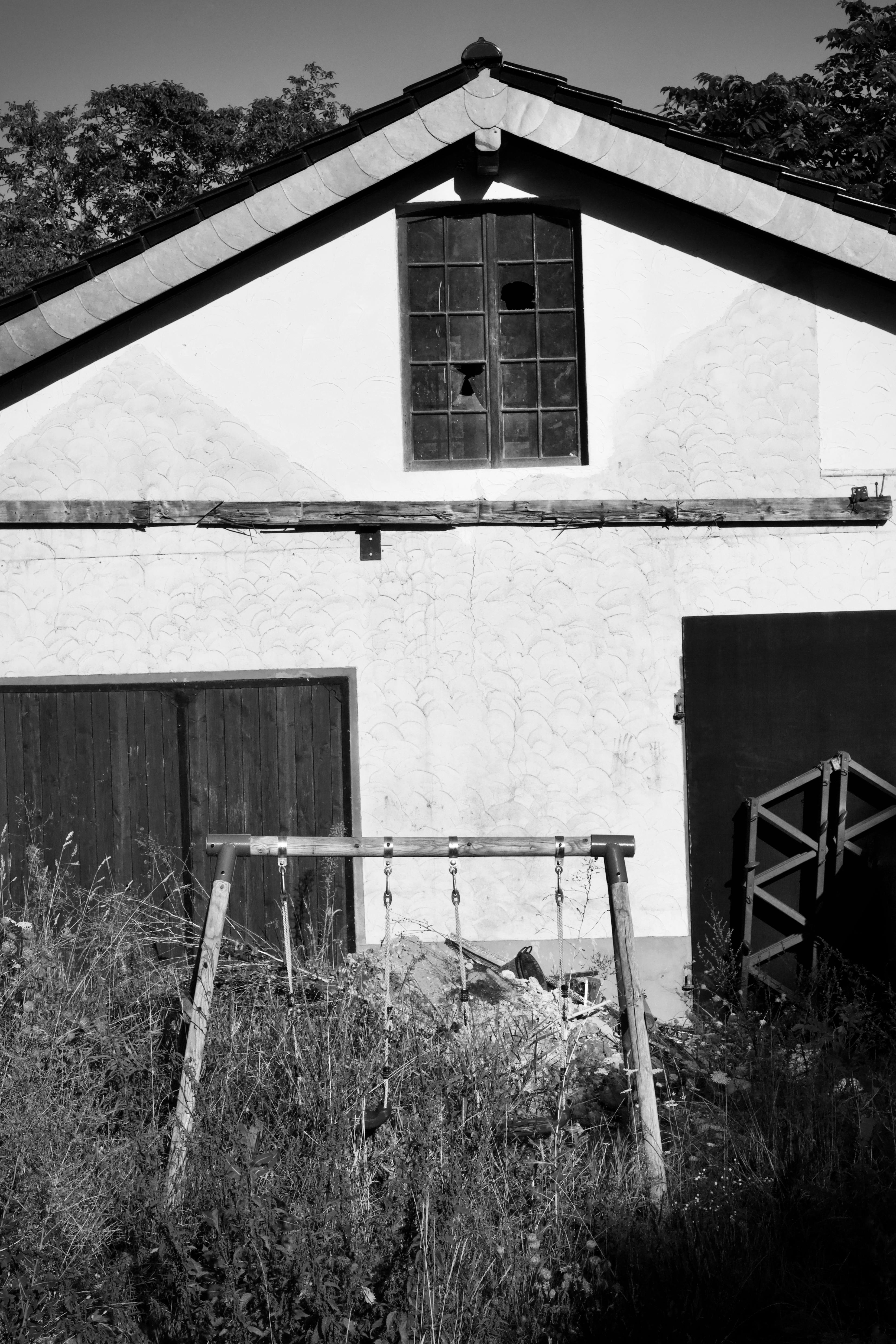 бесплатная Заброшенный, обветшалый дом с разбитыми окнами и разросшейся растительностью в сельской местности. Стоковое фото