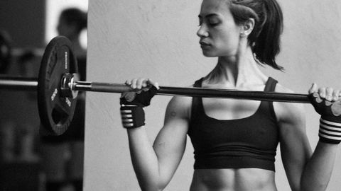 Athletic woman exercising with a barbell for strength training in a gym.