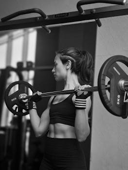 Focused woman lifting barbell in gym. Strength and fitness.