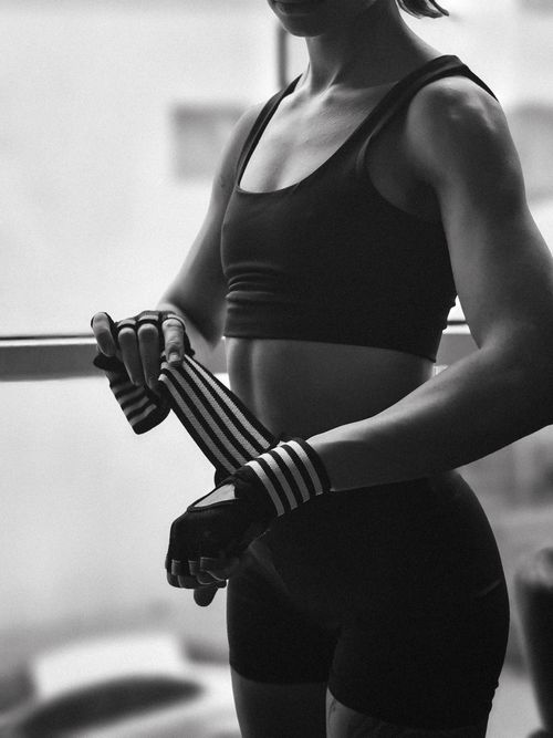 Free Closeup of a woman in sports attire adjusting straps on her gloves, readying for an indoor workout. Stock Photo