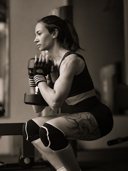Free Determined woman performing strength training with dumbbells in a gym environment. Stock Photo