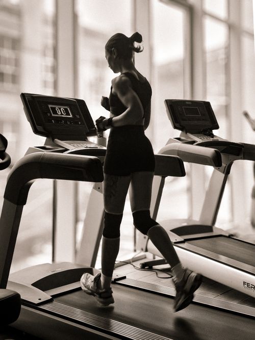 Free A monochrome image of a woman jogging indoors on treadmill with a city view. Stock Photo
