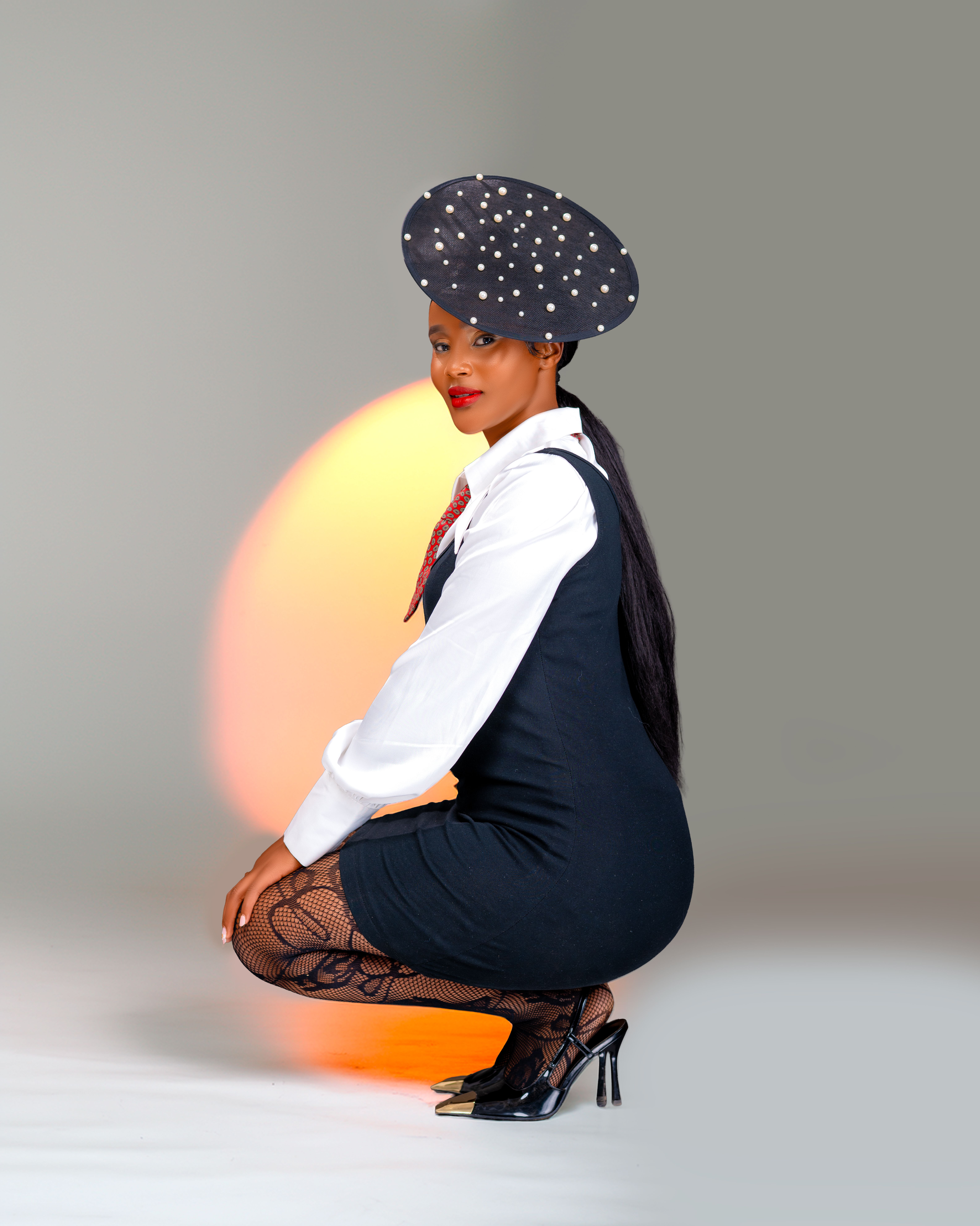 Stylish woman in a black dress with a pearl hat posing elegantly.