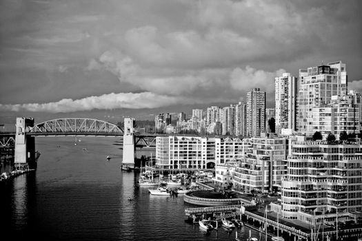 Dramatic black and white view of Vancouver's skyline and Burrard Bridge over water.