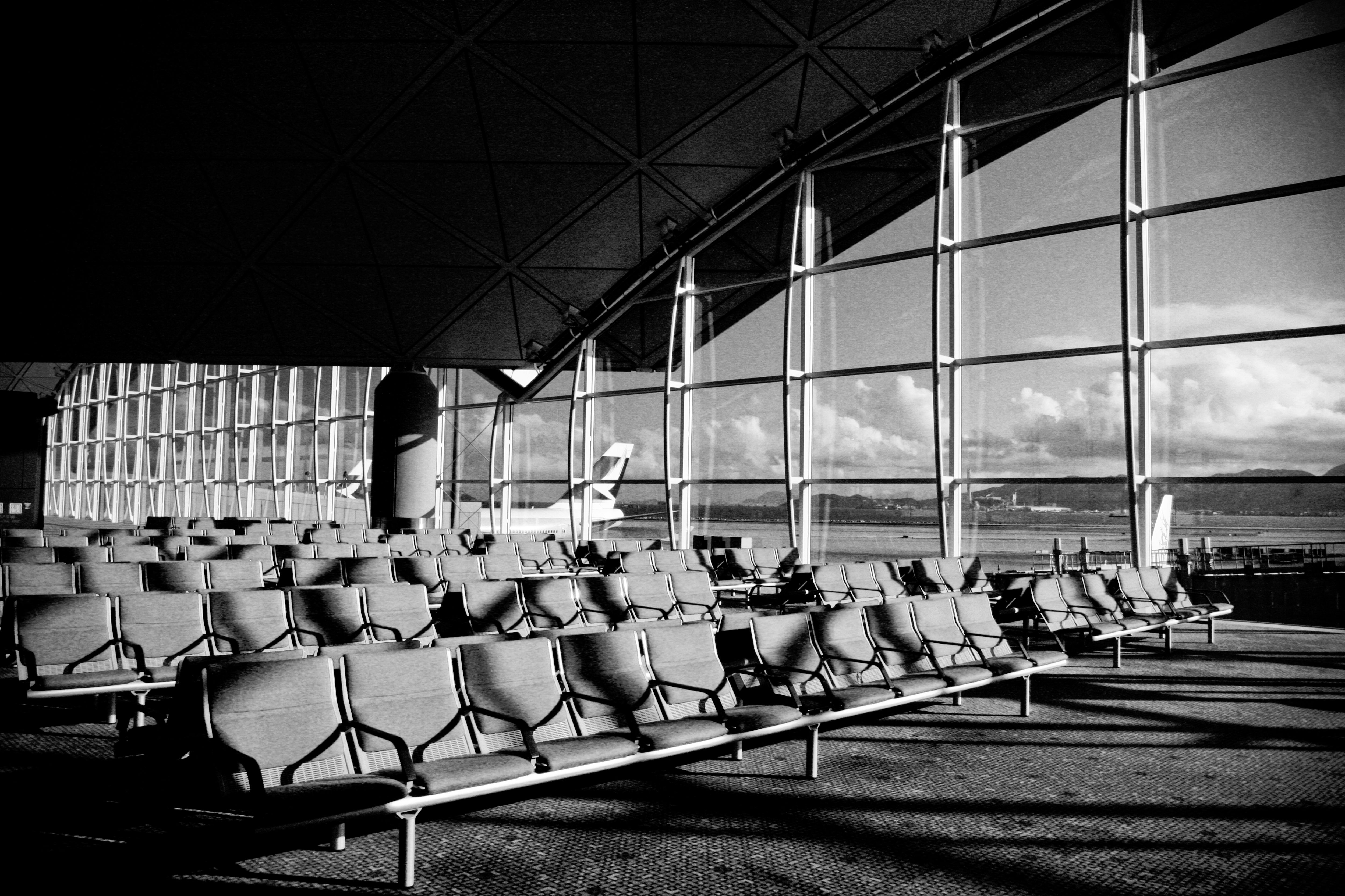 Empty airport terminal with empty seats, large windows, and a distant airplane.