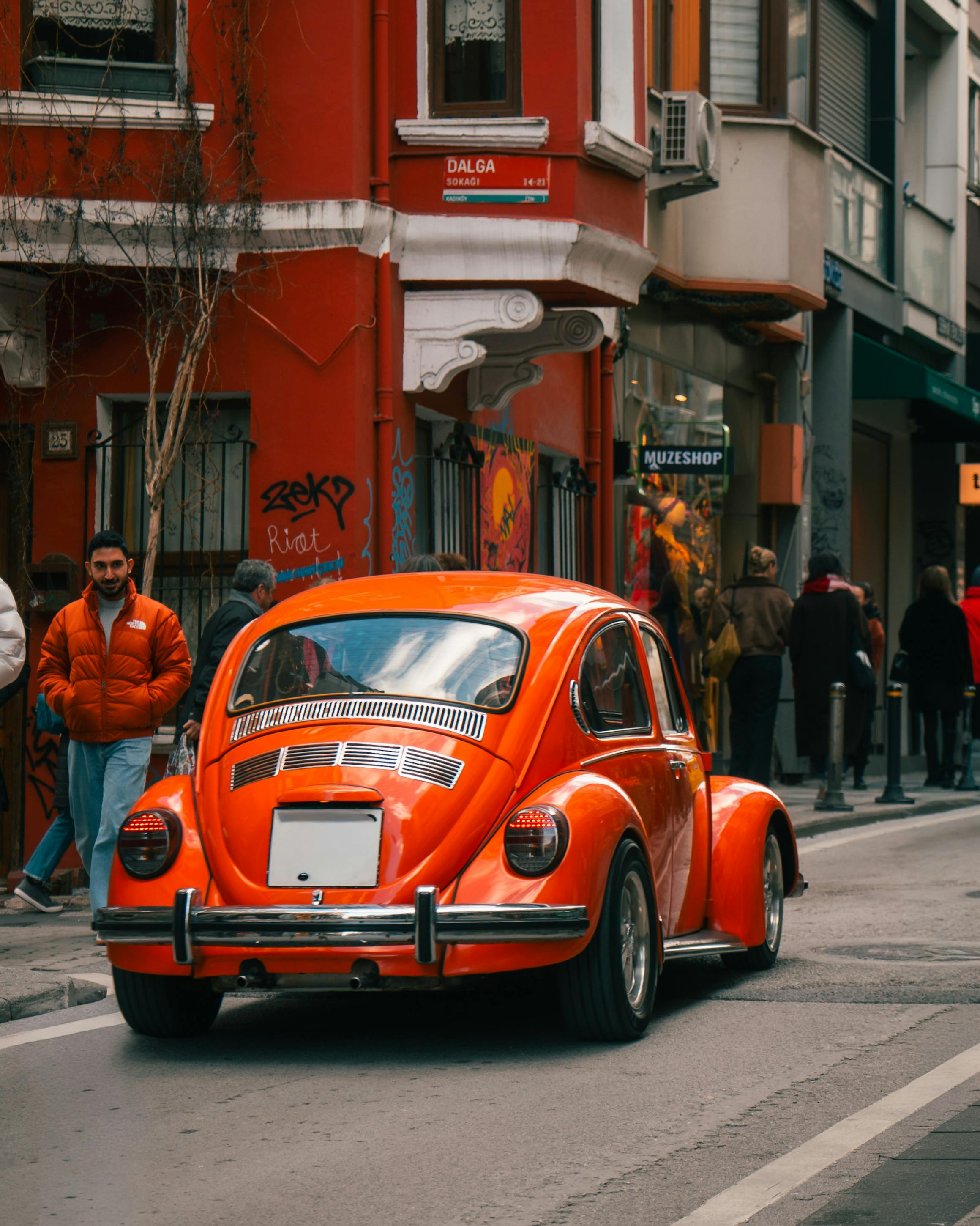無料 活気のある都市を背景に、街の通りに駐車されたビンテージの赤いビートル車。 写真素材
