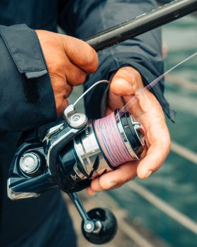 Detailed view of hands managing a fishing reel outdoors, perfect for fishing enthusiasts.