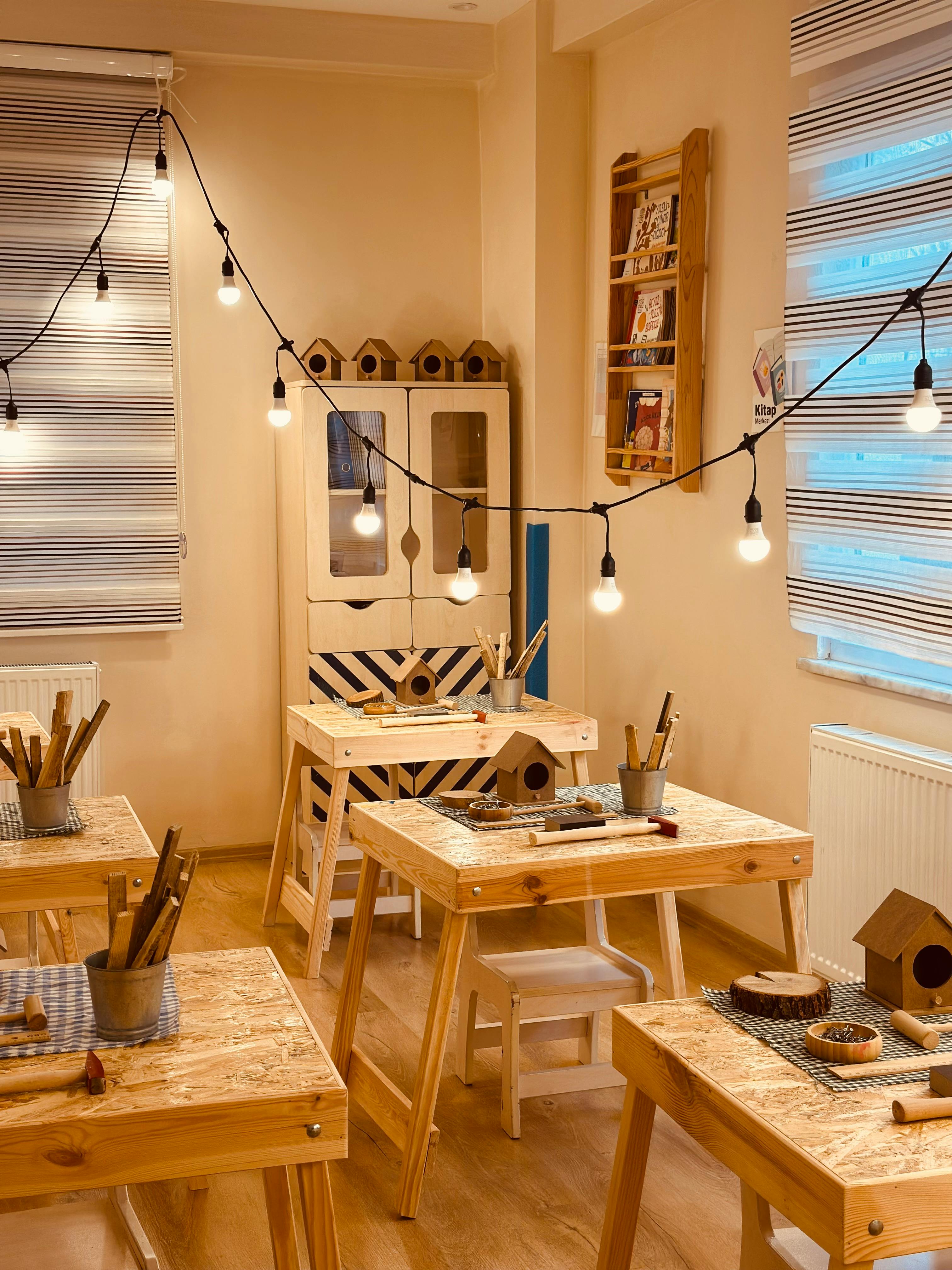 Gratis Varmt og indbydende træbearbejdningsklasseværelse med lyskæder og træborde til håndarbejdsaktiviteter. Lagerfoto