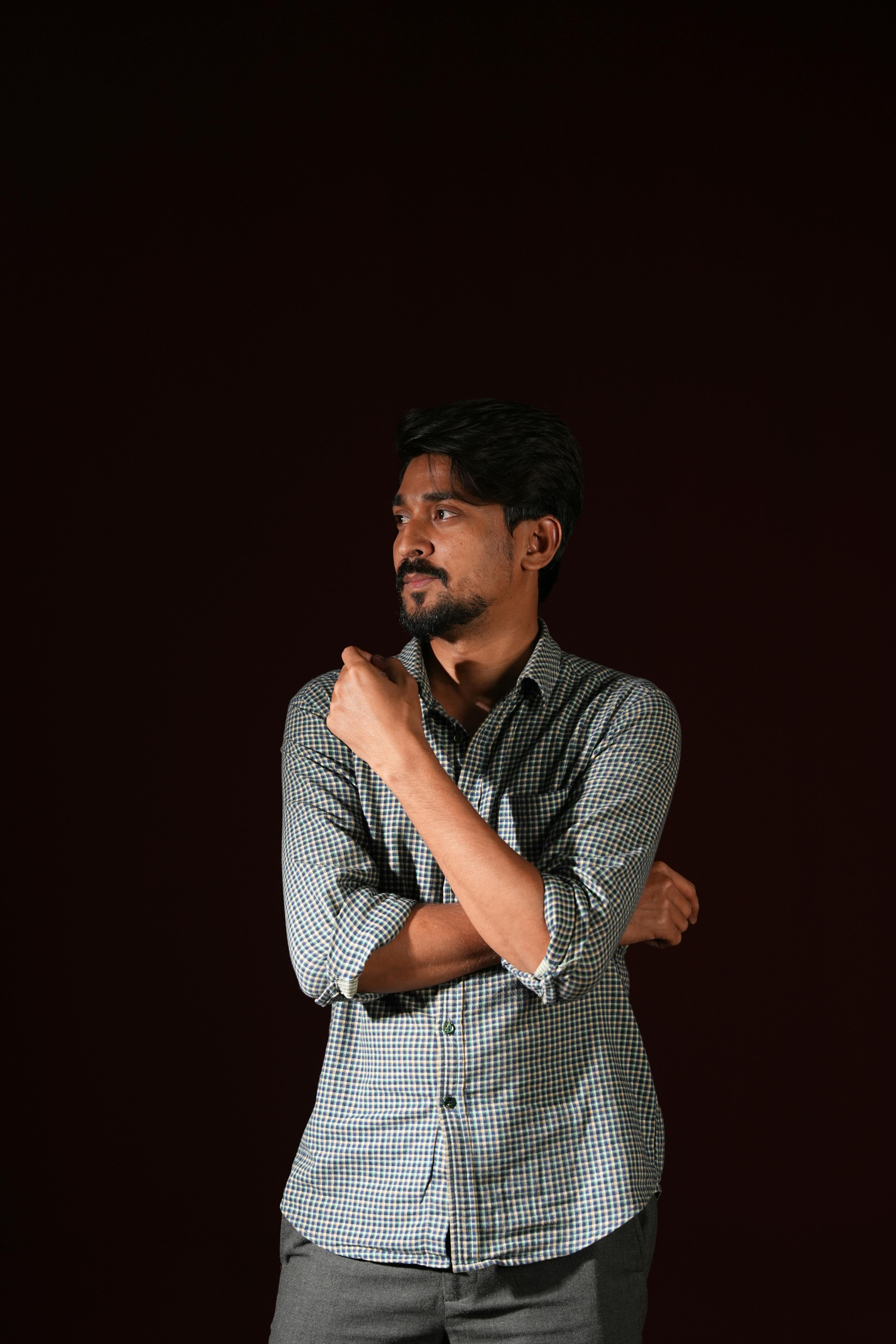 A thoughtful man in a checkered shirt poses against a dark background, showing a contemplative expression.