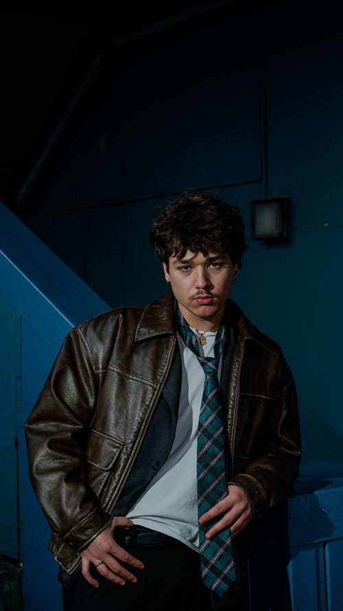 Free Portrait of a young man in a brown leather jacket with a blue background, exuding a confident vibe. Stock Photo