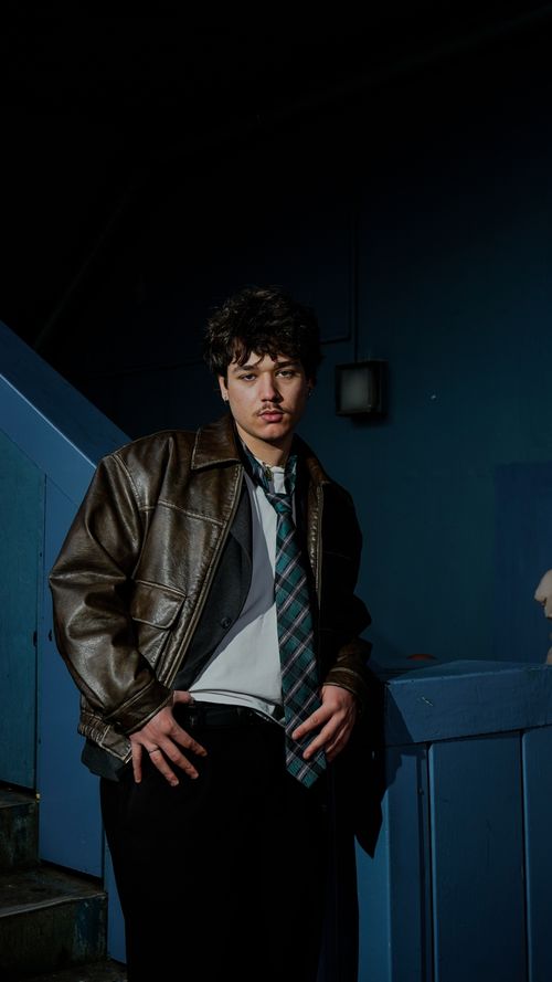 Free Fashionable man in leather jacket poses indoors in low light, showcasing modern style. Stock Photo