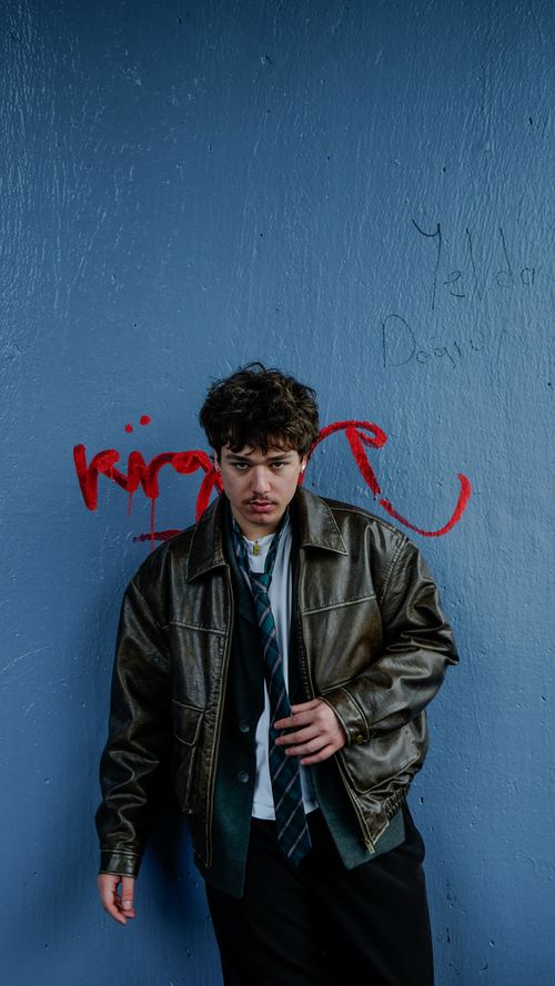 Free Young man in leather jacket and tie posing against a graffiti wall. Urban fashion and style concept. Stock Photo