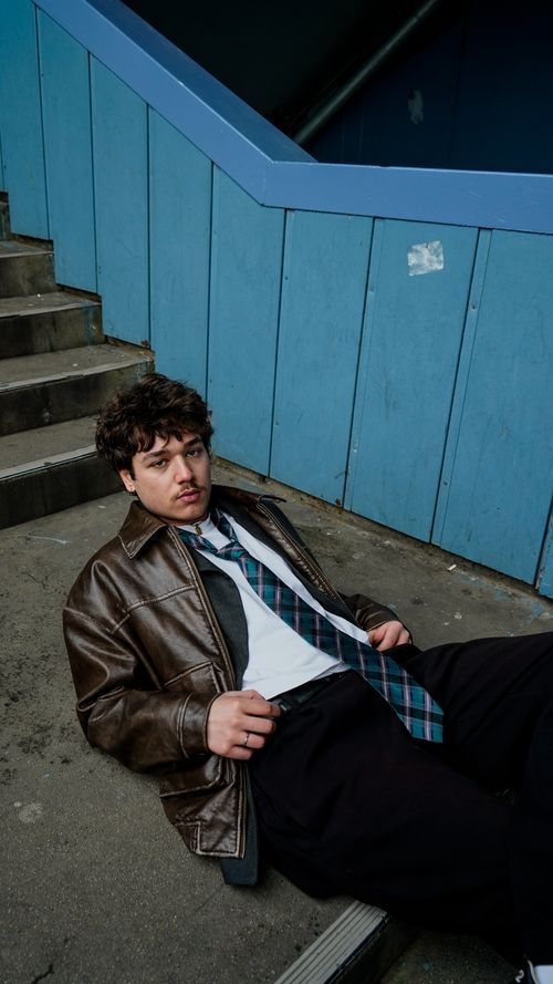 Free Young man in leather jacket relaxing on stairway steps in an urban setting. Stock Photo