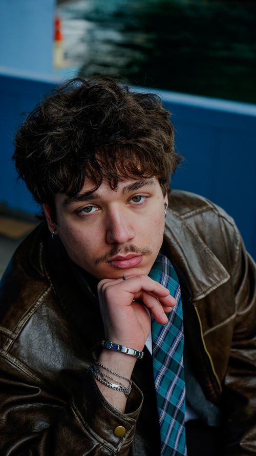 Free Portrait of a young man in a leather jacket with a contemplative expression by the water. Stock Photo