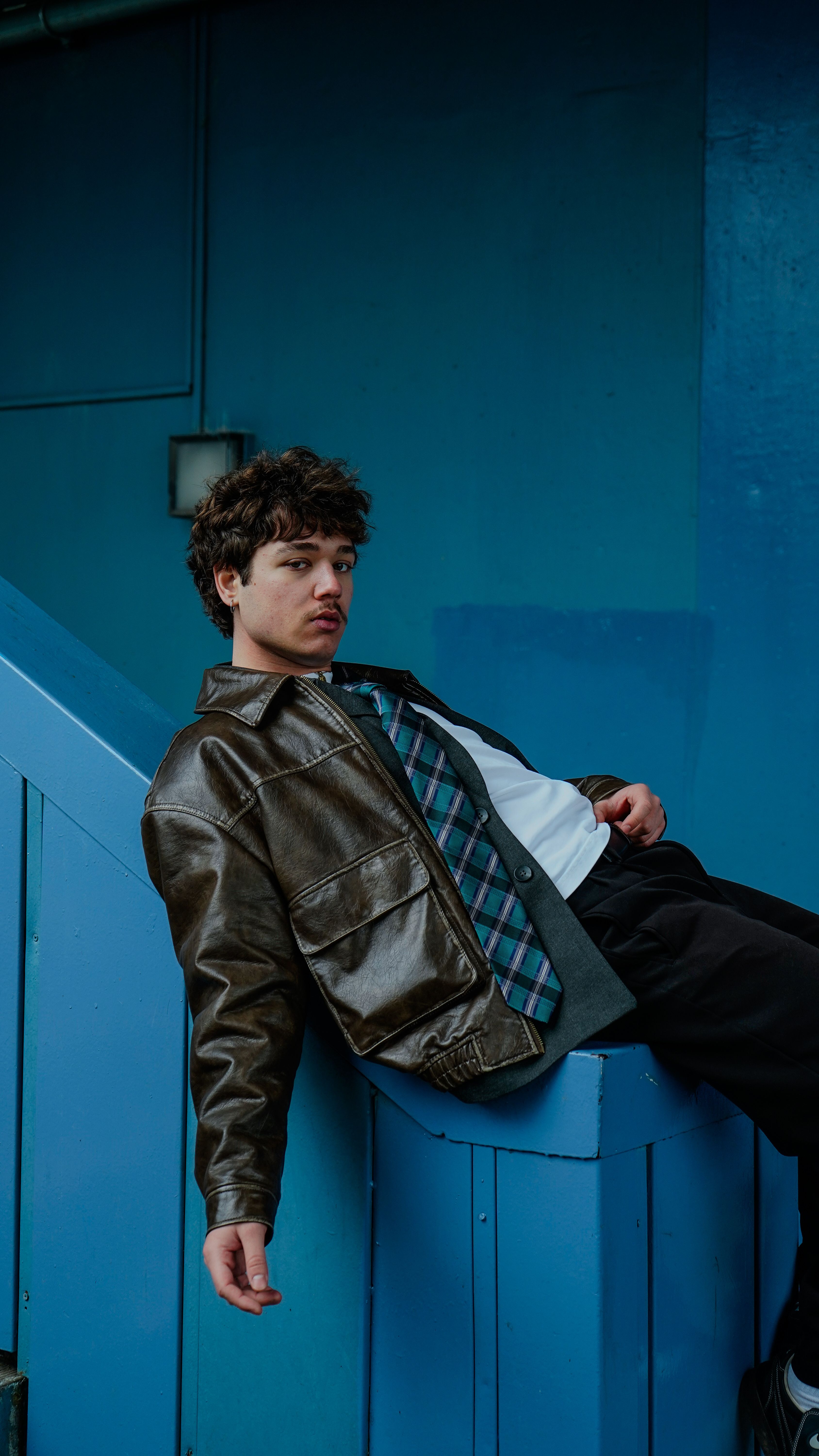 Trendy young man in a leather jacket posing against a blue background.