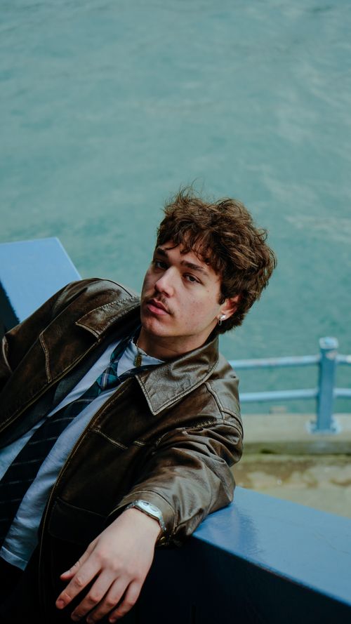 Free Young man in a leather jacket leaning on a railing by the sea on a cool day. Stock Photo