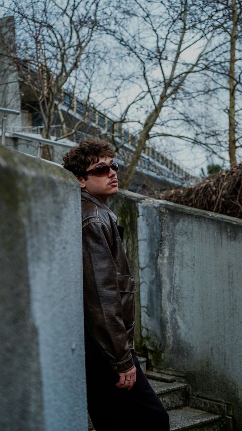 Free Stylish young adult wearing sunglasses and leather jacket in an urban setting, exuding a cool and modern vibe. Stock Photo