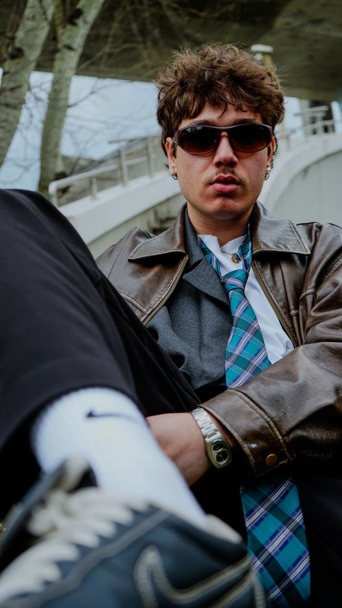 Free Stylish young man in sunglasses and leather jacket lounging outdoors, exuding a cool vibe. Stock Photo