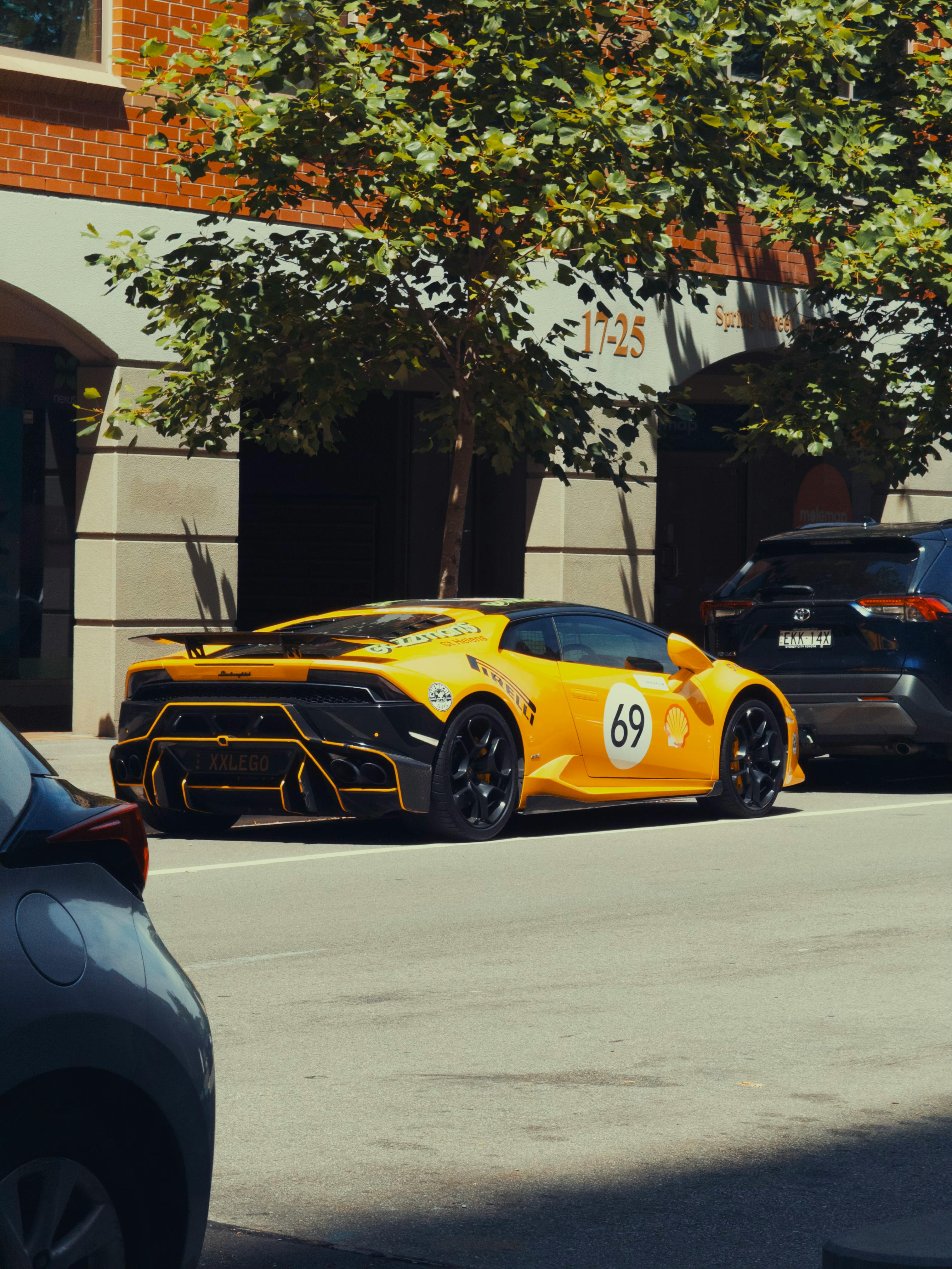 無料 レーシングデカールが付いた鮮やかな黄色のスポーツカーが都会の路上に駐車されています。 写真素材