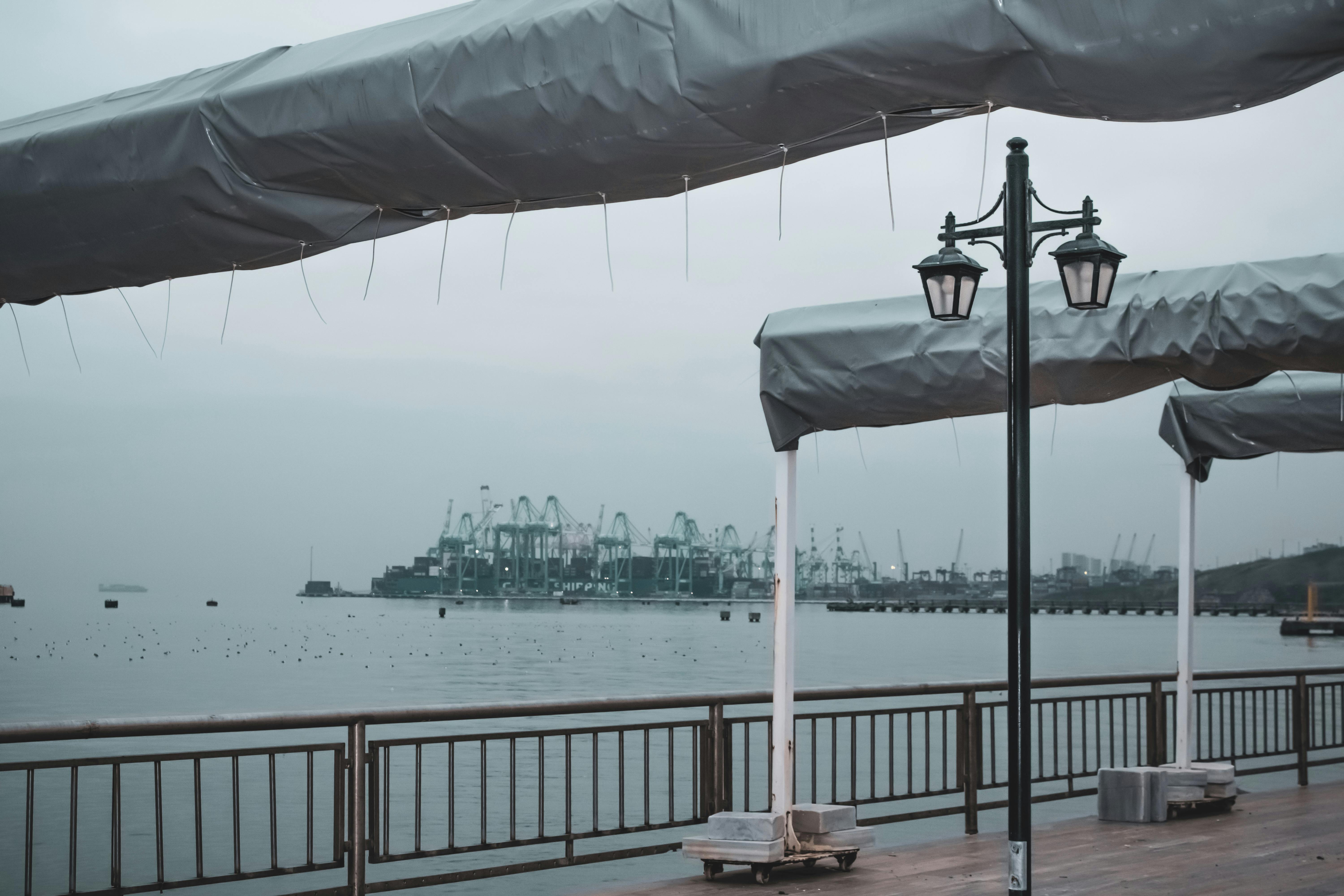 無料 曇り空の下、穏やかな雰囲気の工業用クレーンのある静かなウォーターフロント。 写真素材