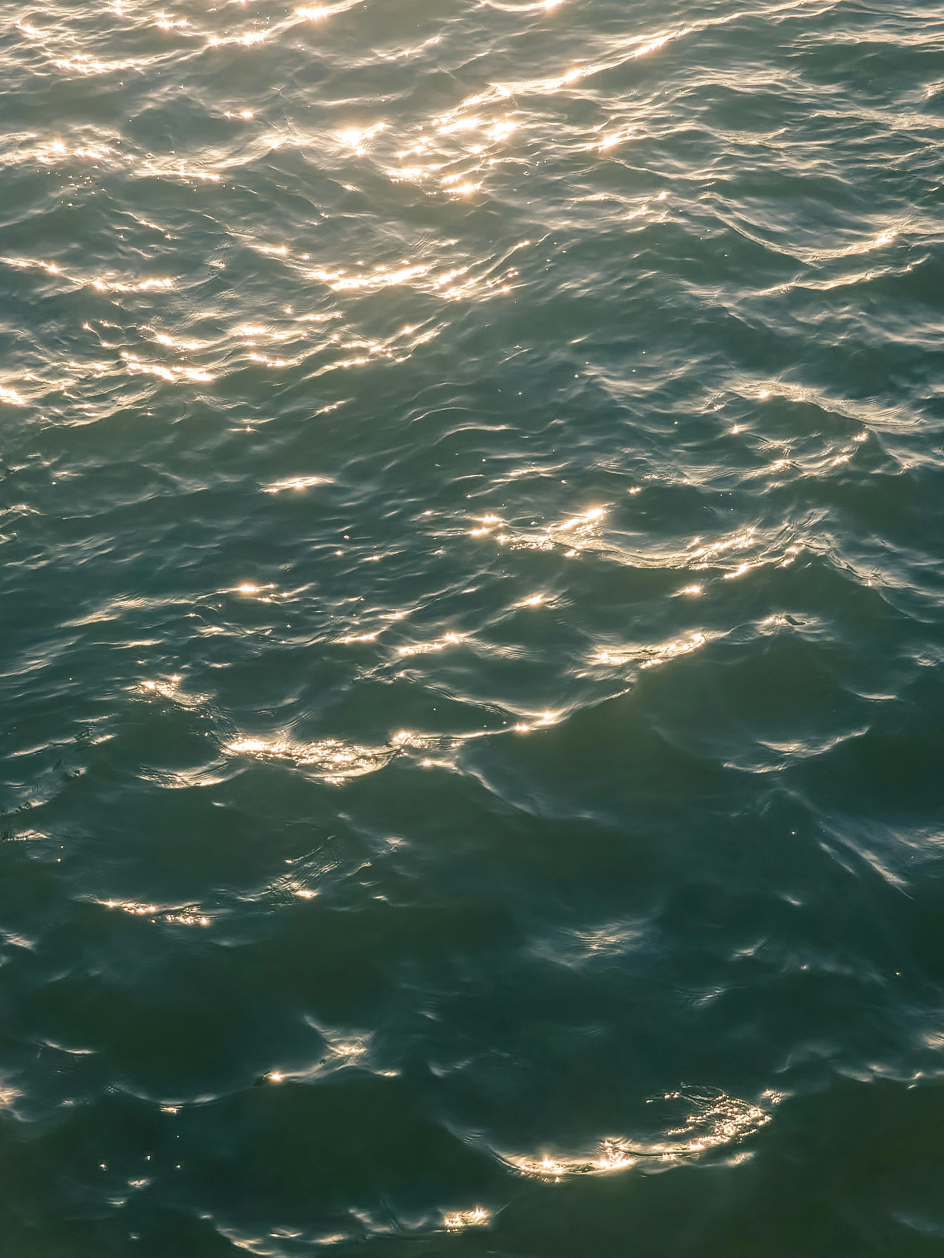 無料 暖かい太陽の光の下で穏やかな海の波がきらめき、心安らぐ平和な光景を作り出しています。 写真素材