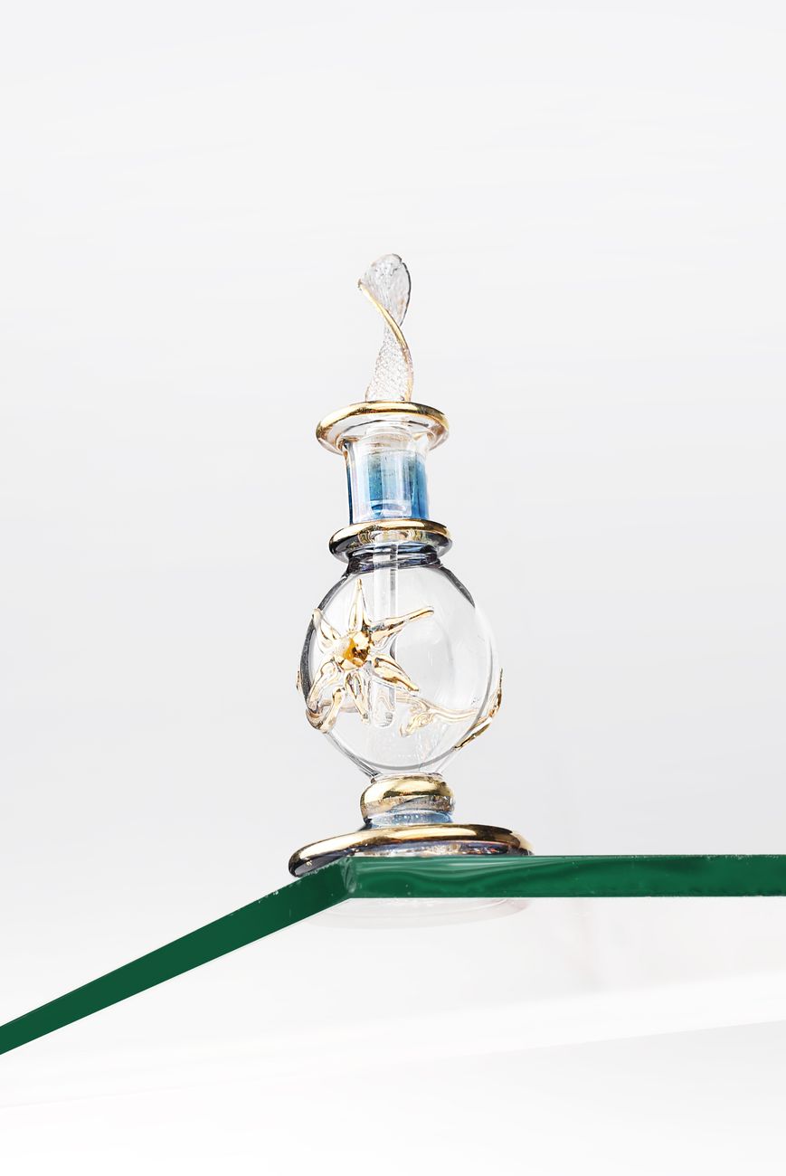 Ornate glass perfume bottle with golden design on a glass shelf.