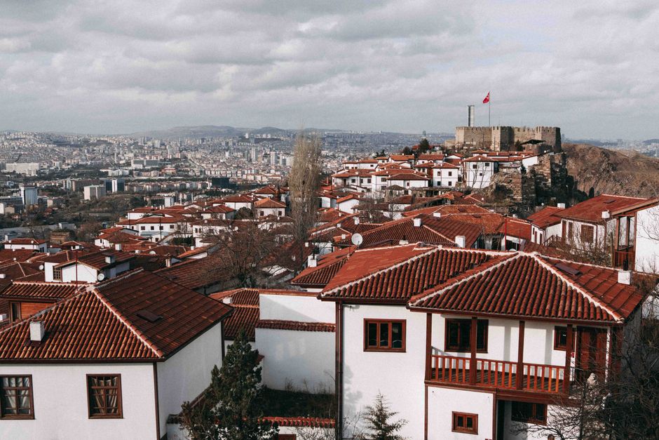 Aerial view of Ankara's traditional red rooftops and historic castle under a cloudy sky.