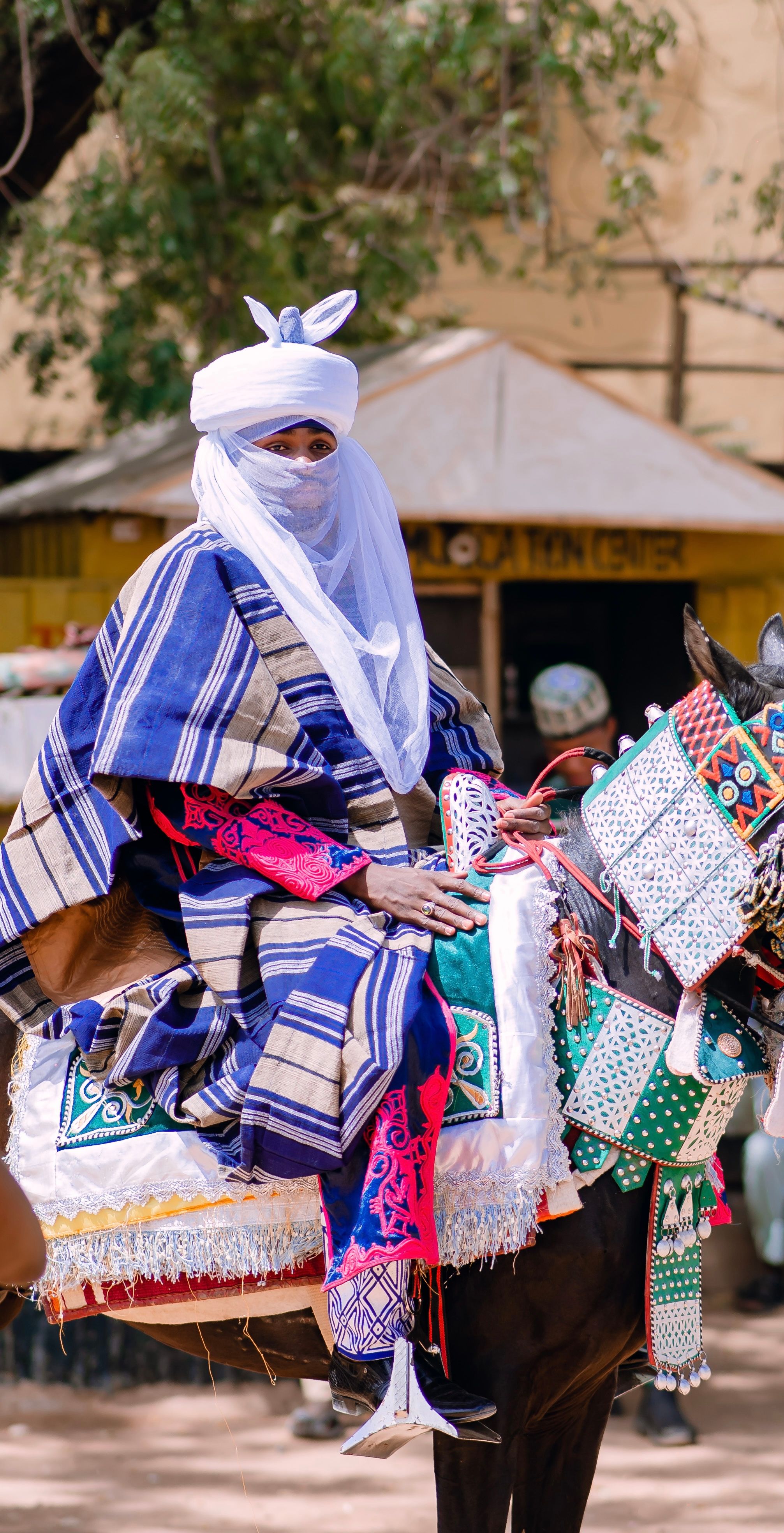 A Nigerian horseman in cultural attire riding a decorated horse in a vibrant setting.
