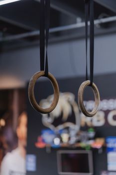 Close-up of hanging wooden gymnastic rings in a modern fitness gym setting.