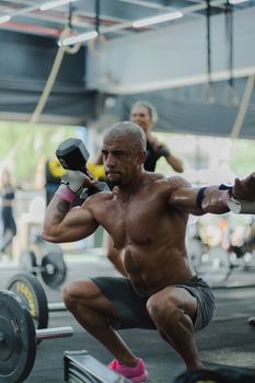 A muscular man performing a squat with a dumbbell in an indoor gym setting, showcasing strength and focus.