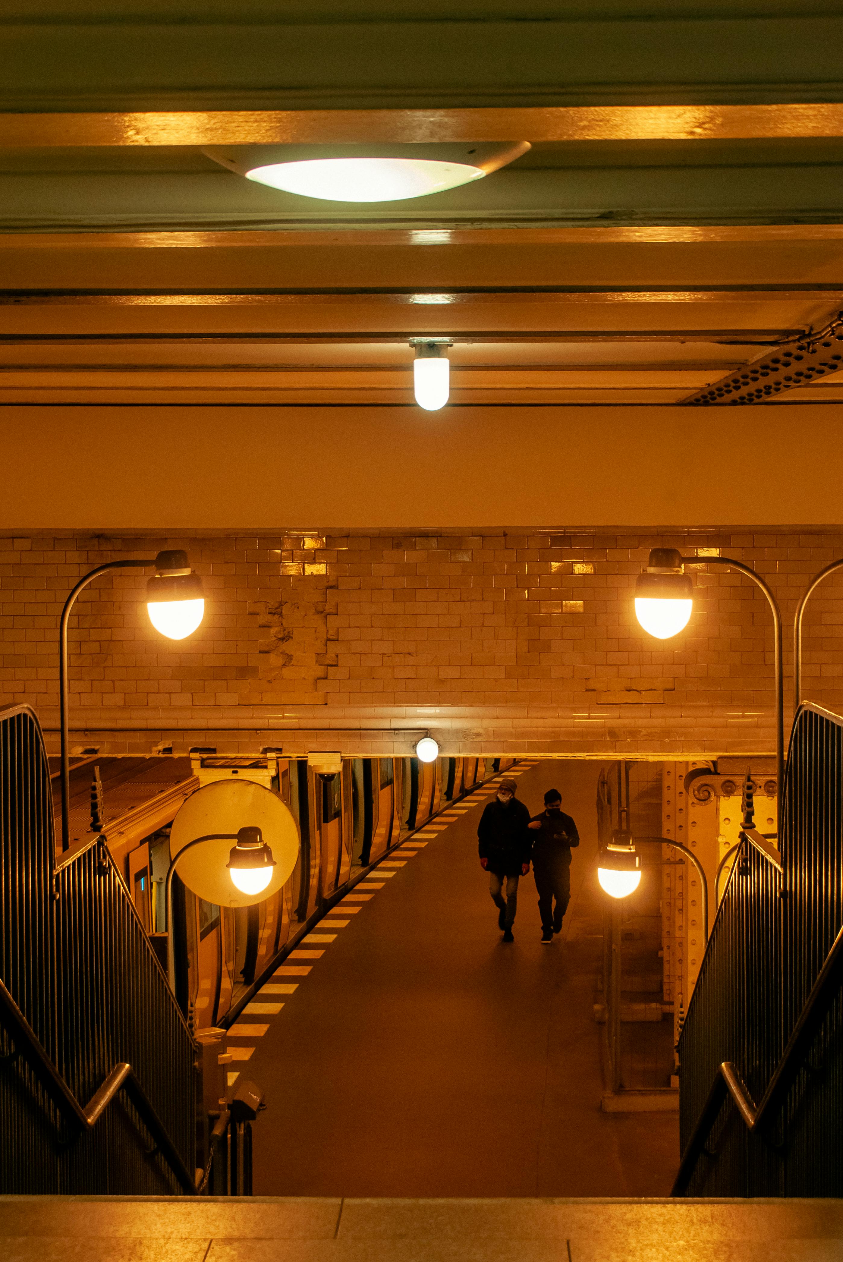 Free Warmly lit urban subway station with two people walking on the platform. Stock Photo