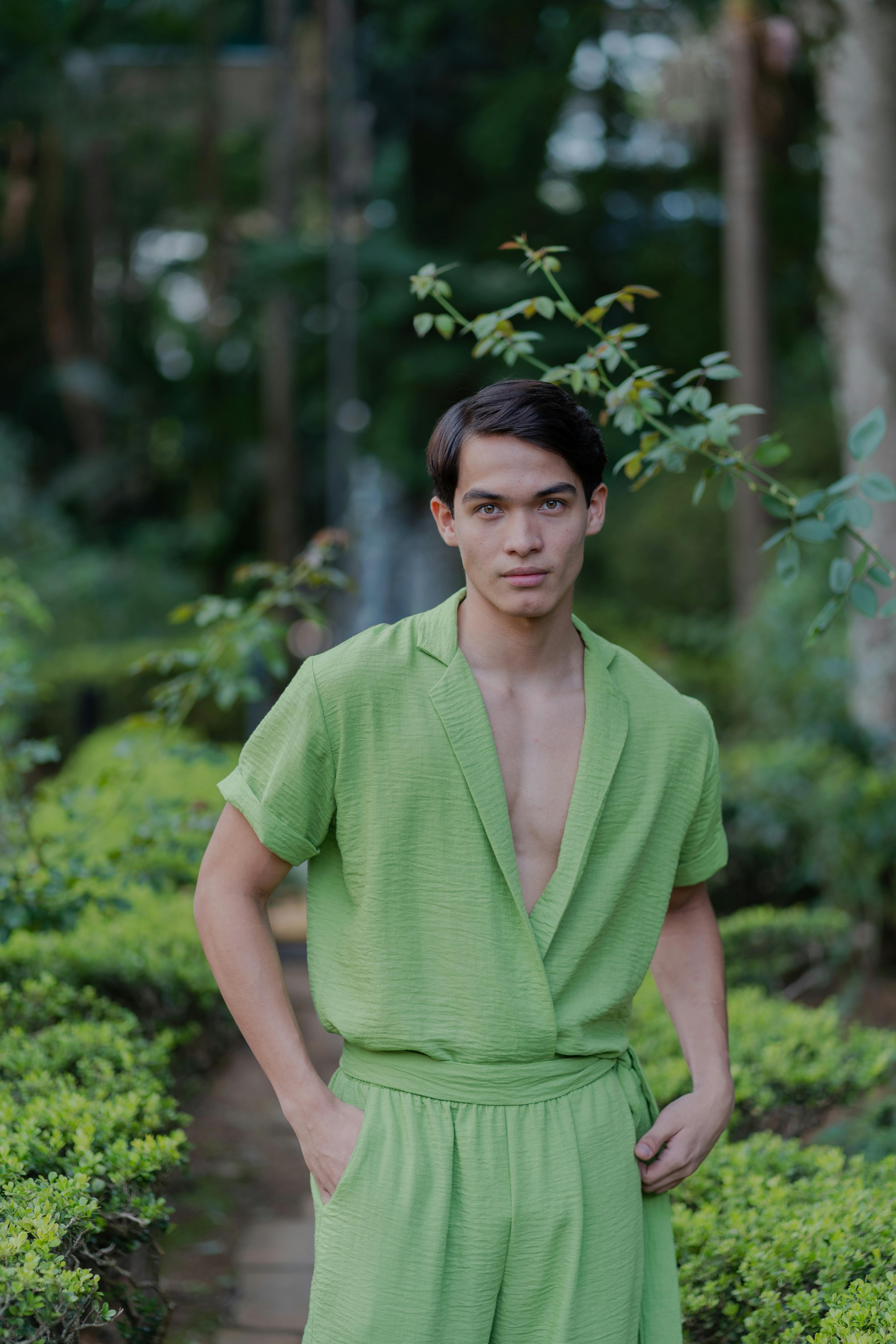 Free A young man in a green outfit poses confidently in a lush outdoor setting. Stock Photo