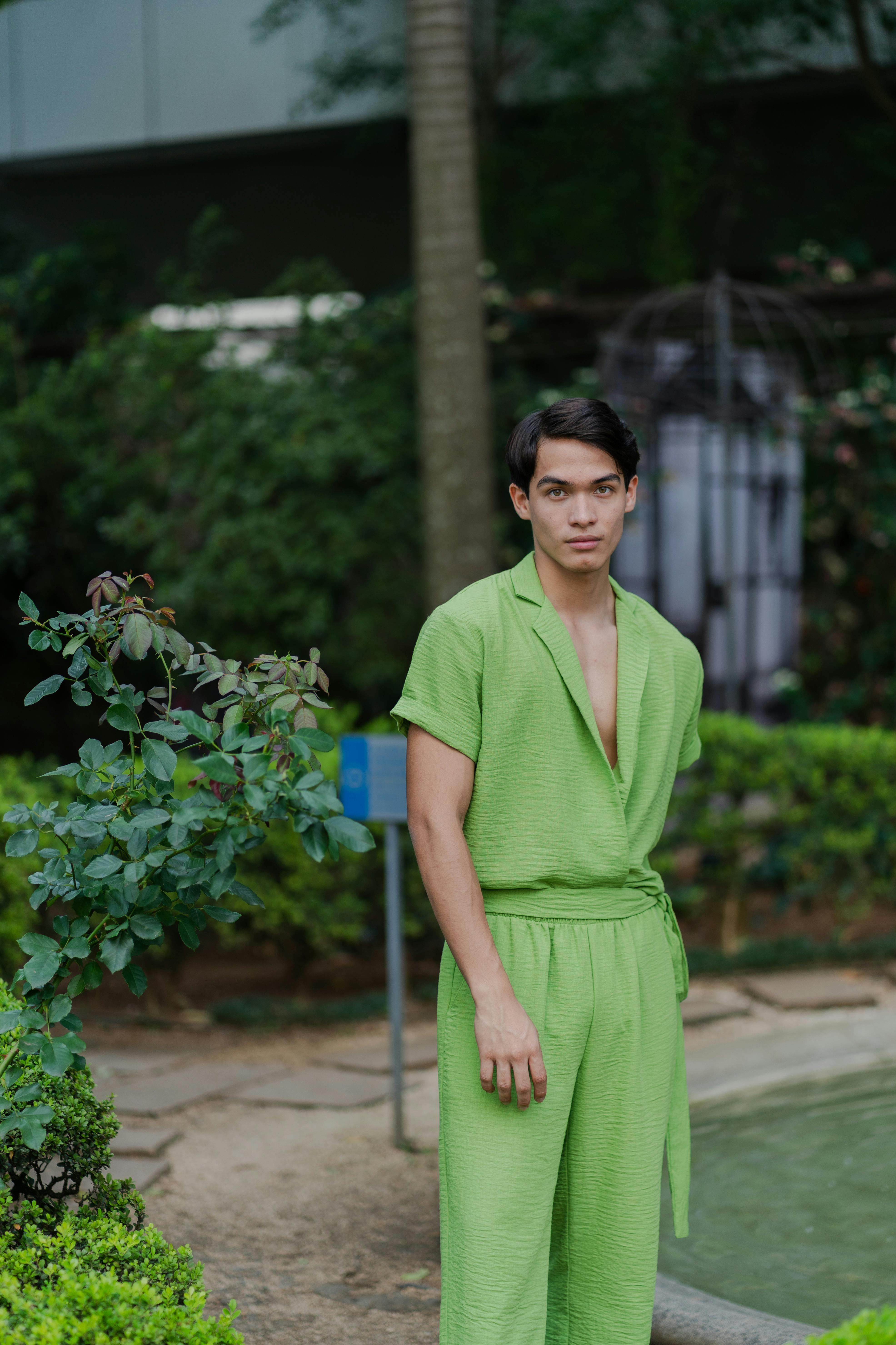 Free A young man in a bright green outfit stands confidently in a lush outdoor setting. Stock Photo