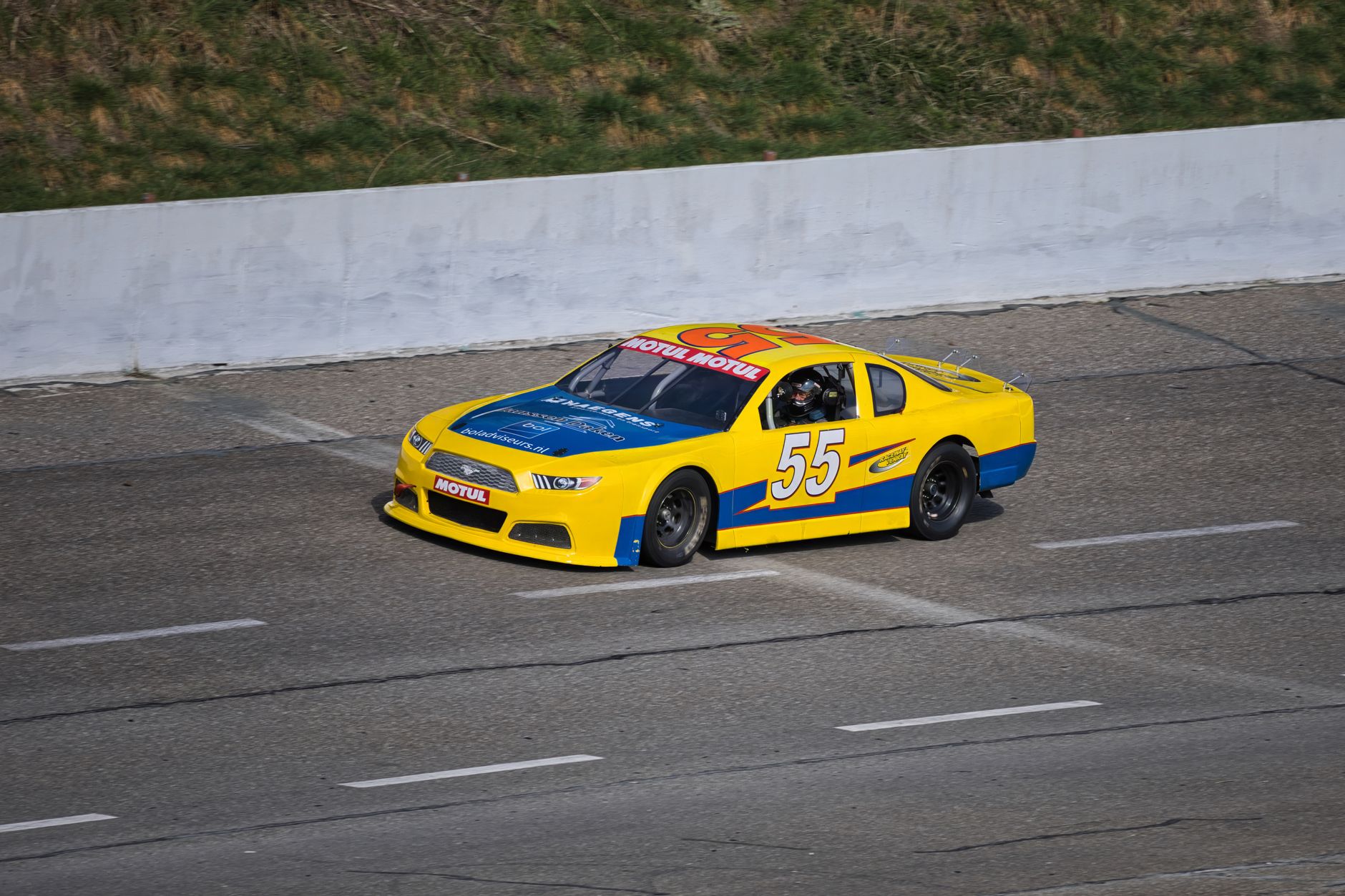 A vibrant yellow and blue stock car racing on an outdoor track during daytime.