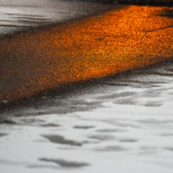 Orange streetlight glowing on wet pavement creating a moody urban reflection.