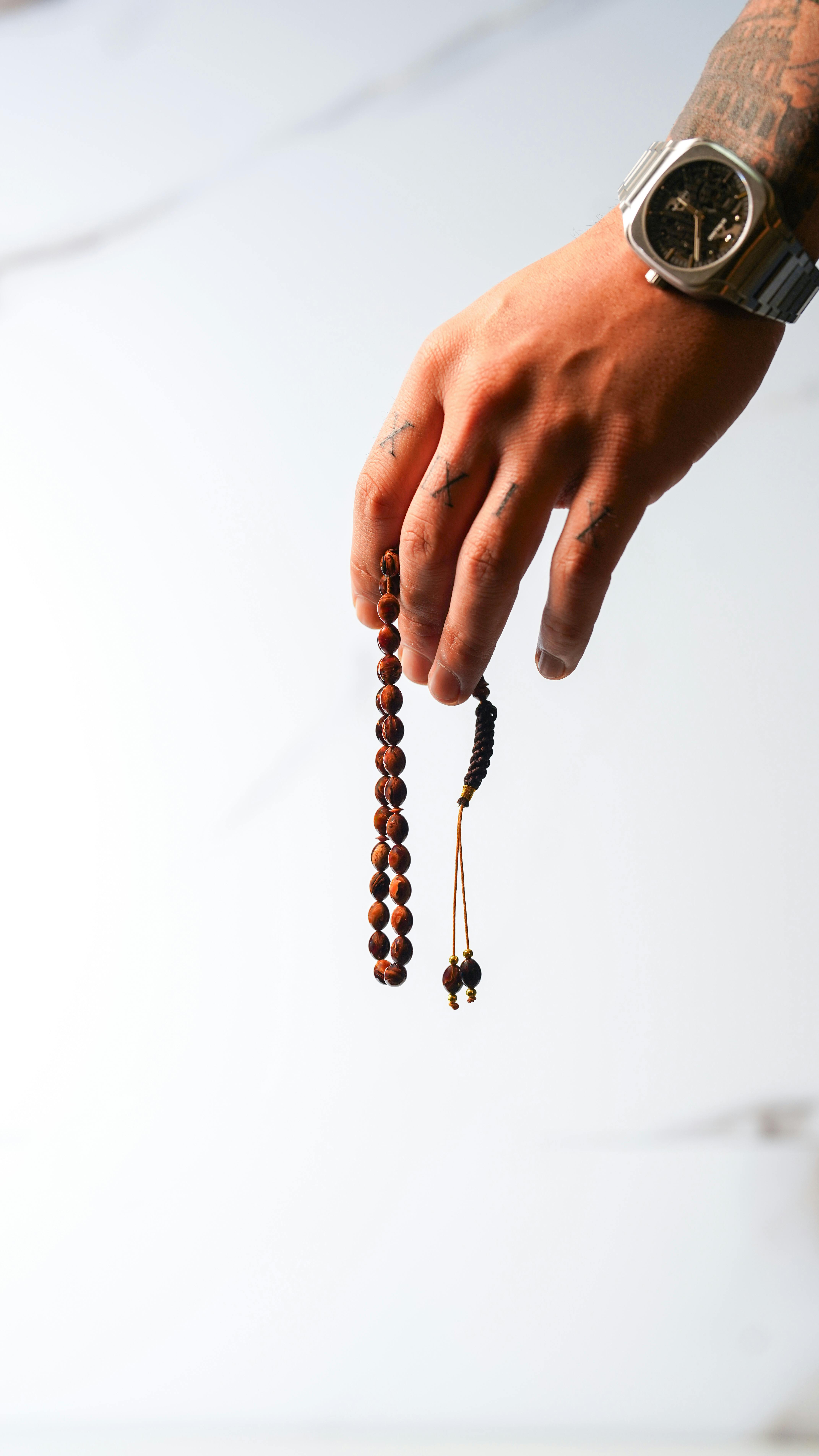 Free A tattooed hand with a watch holding wooden prayer beads against a light background. Stock Photo